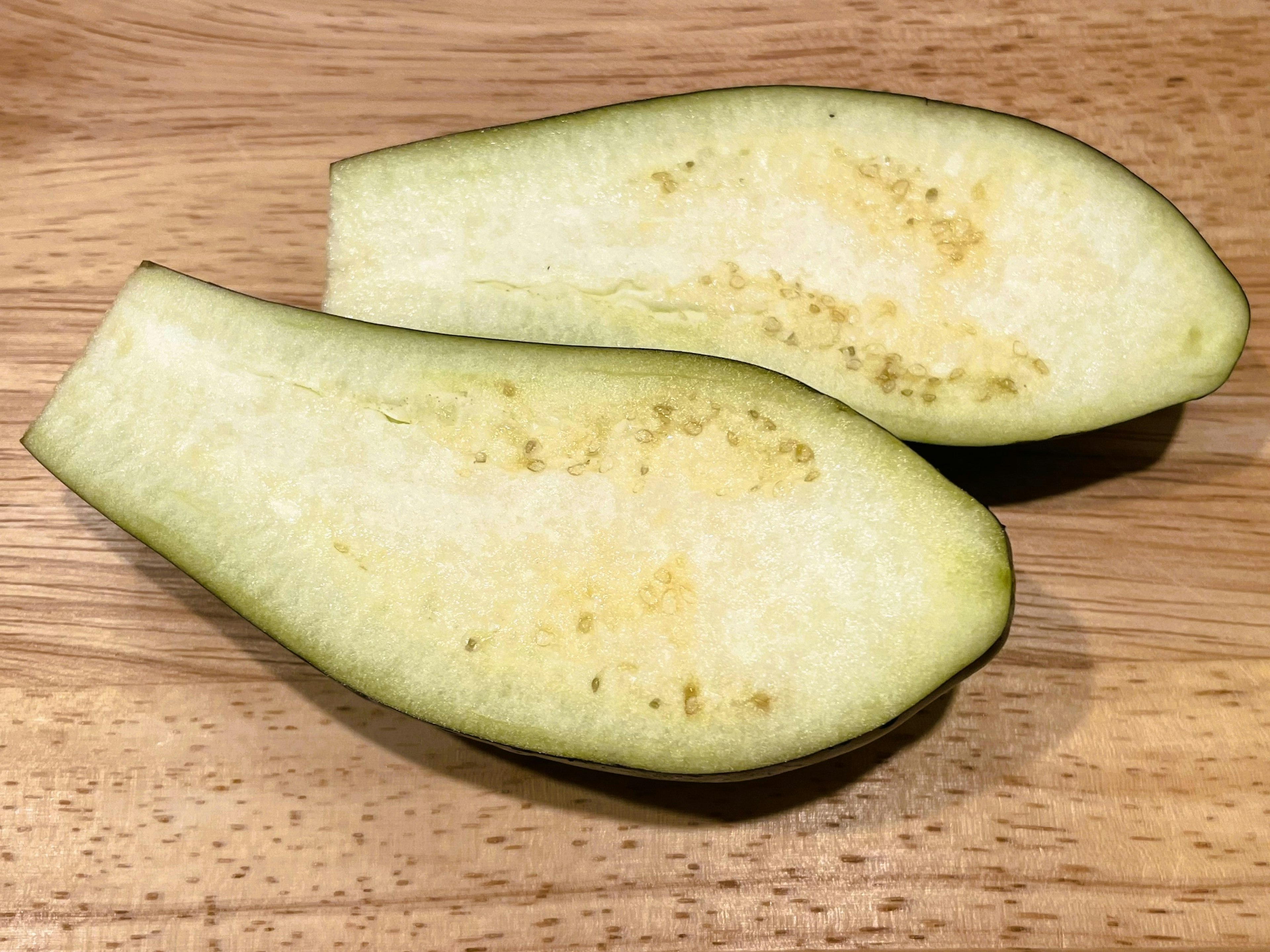 Halved green eggplant on a wooden cutting board