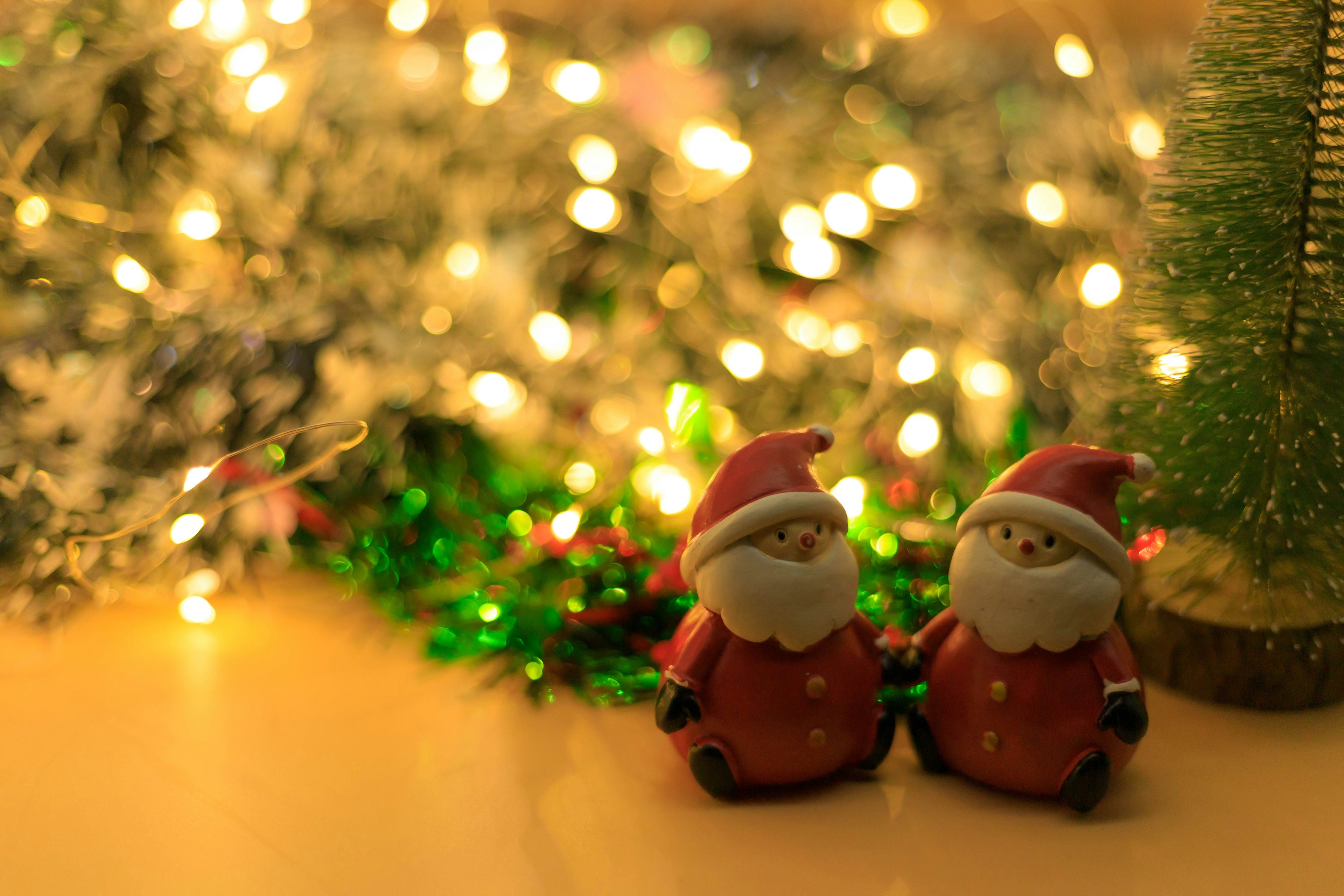 Two Christmas Santa figurines in front of glowing lights