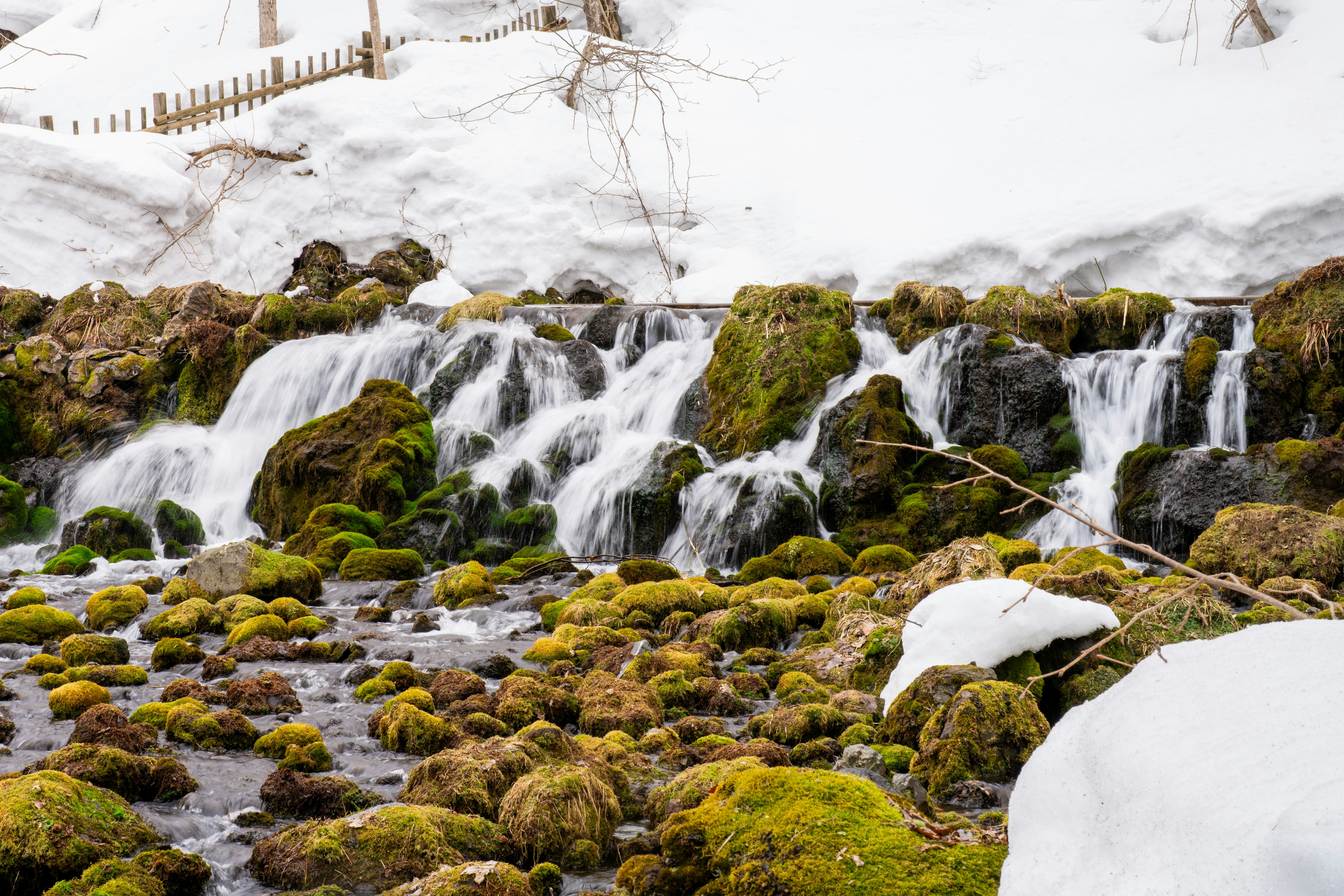 Un arroyo que fluye a través de un paisaje nevado con rocas cubiertas de musgo