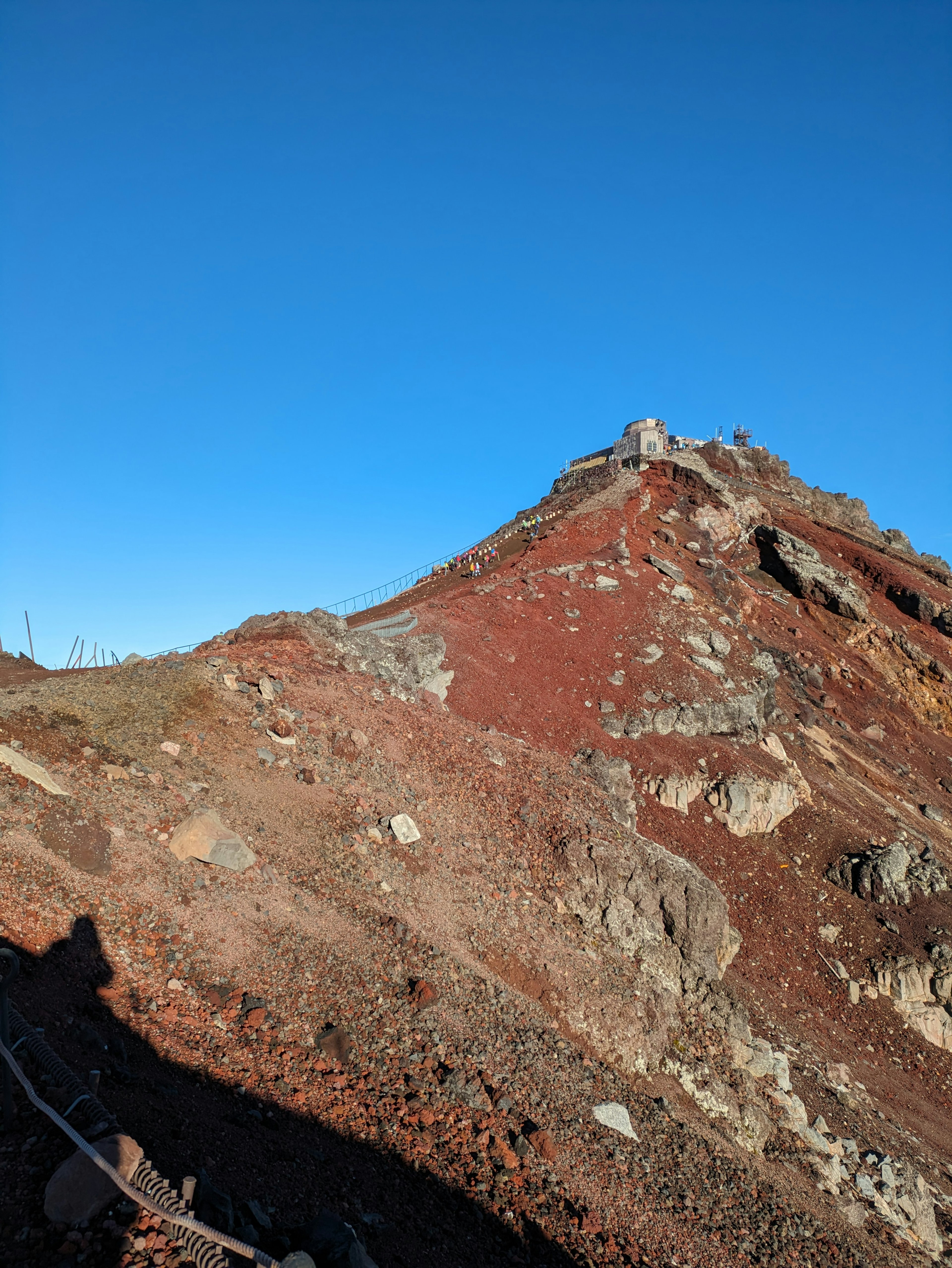 青空の下にある赤い山の頂上に小さな建物が見える