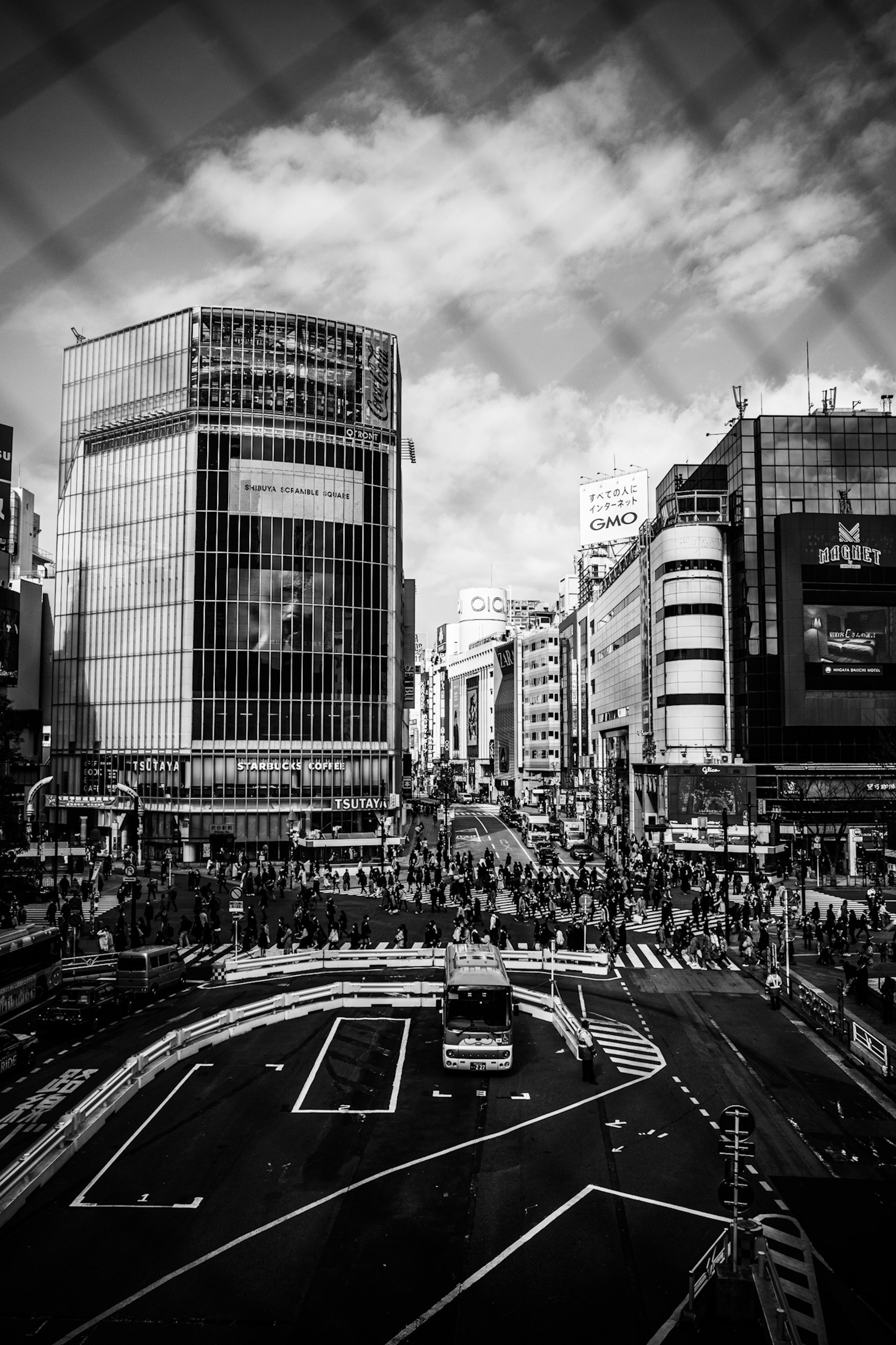 Foto hitam putih Shibuya menunjukkan jalan sibuk dengan banyak pejalan kaki dan kendaraan