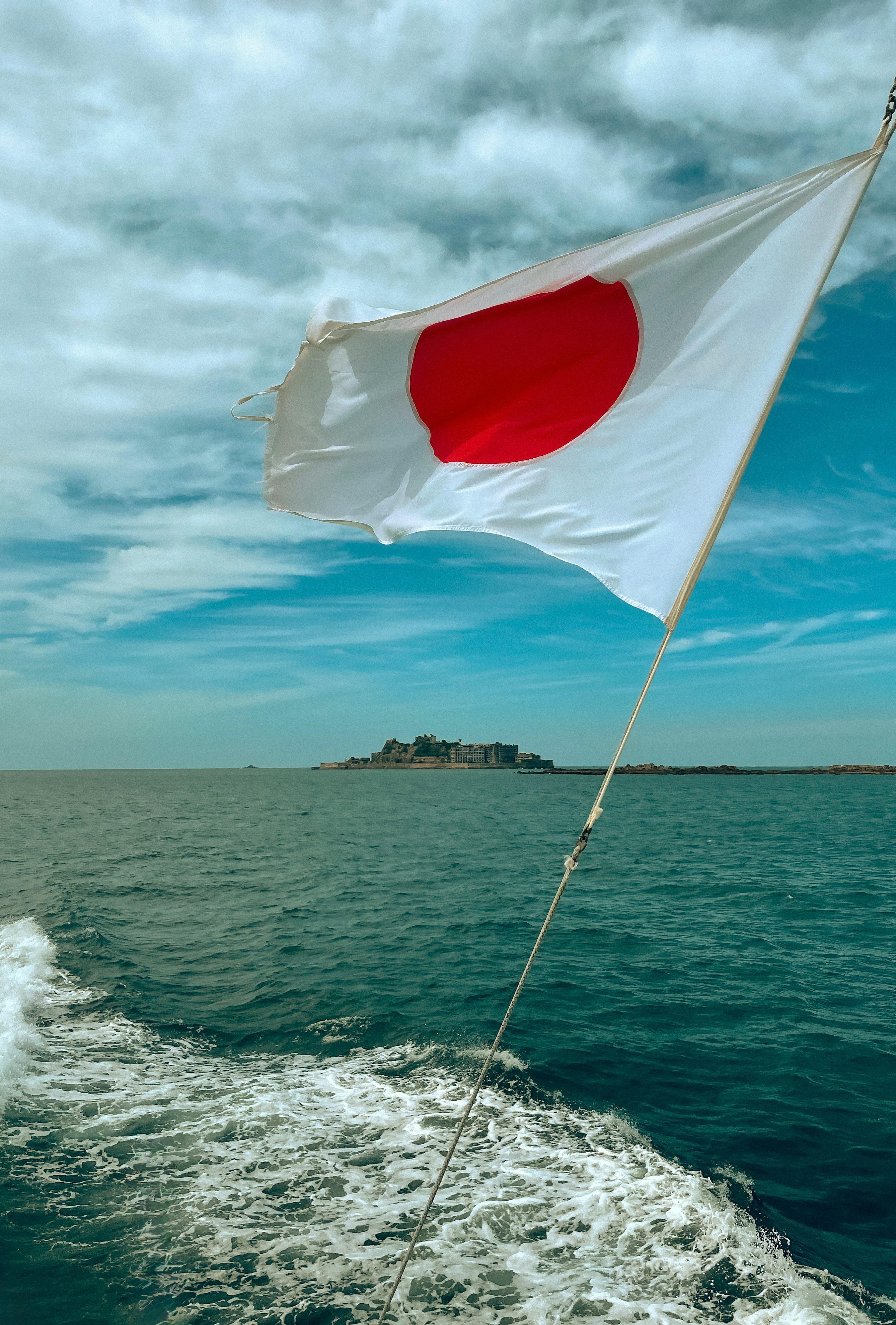 Bendera Jepang berkibar di atas laut dengan pulau di kejauhan