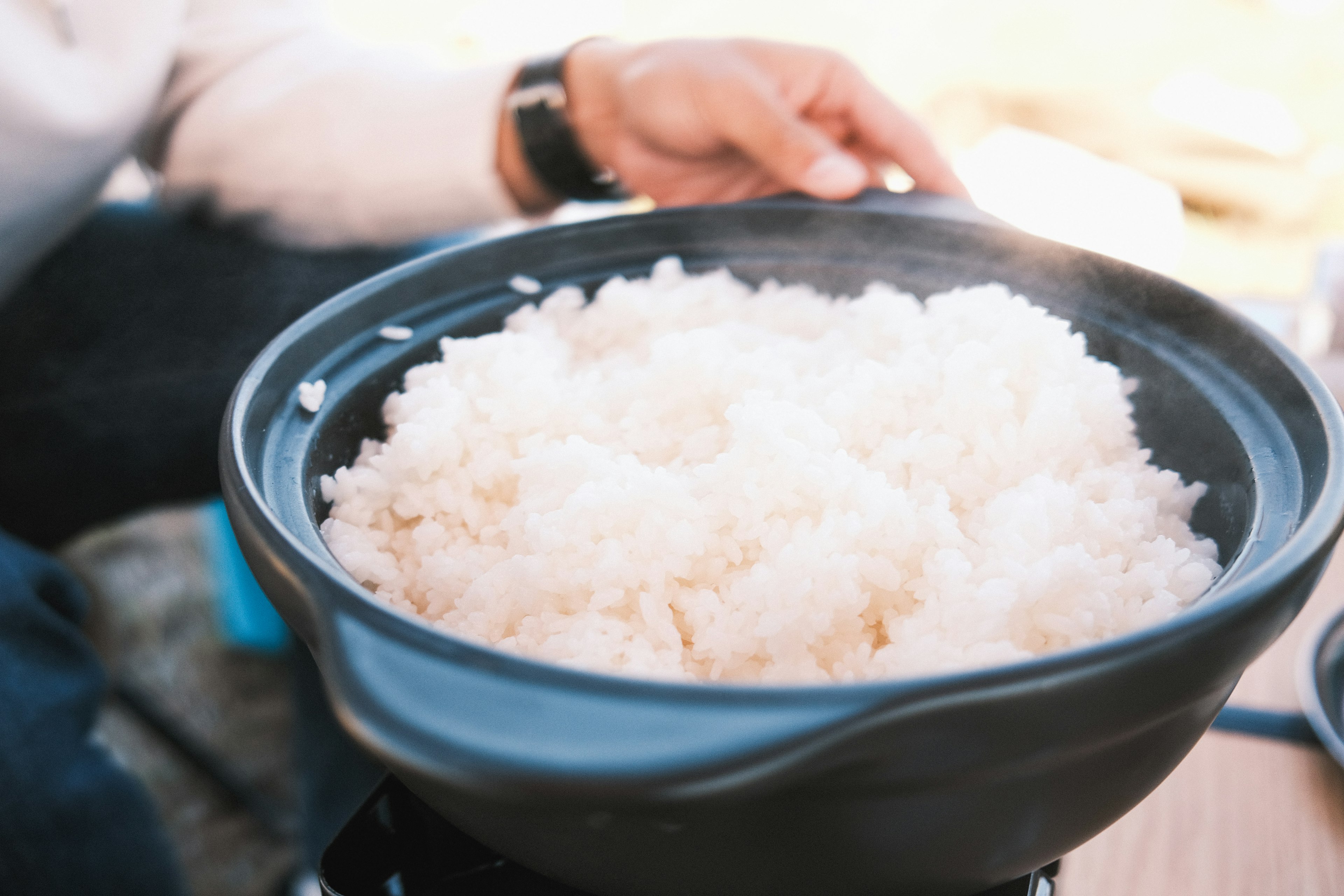 Hand holding a steaming bowl of white rice