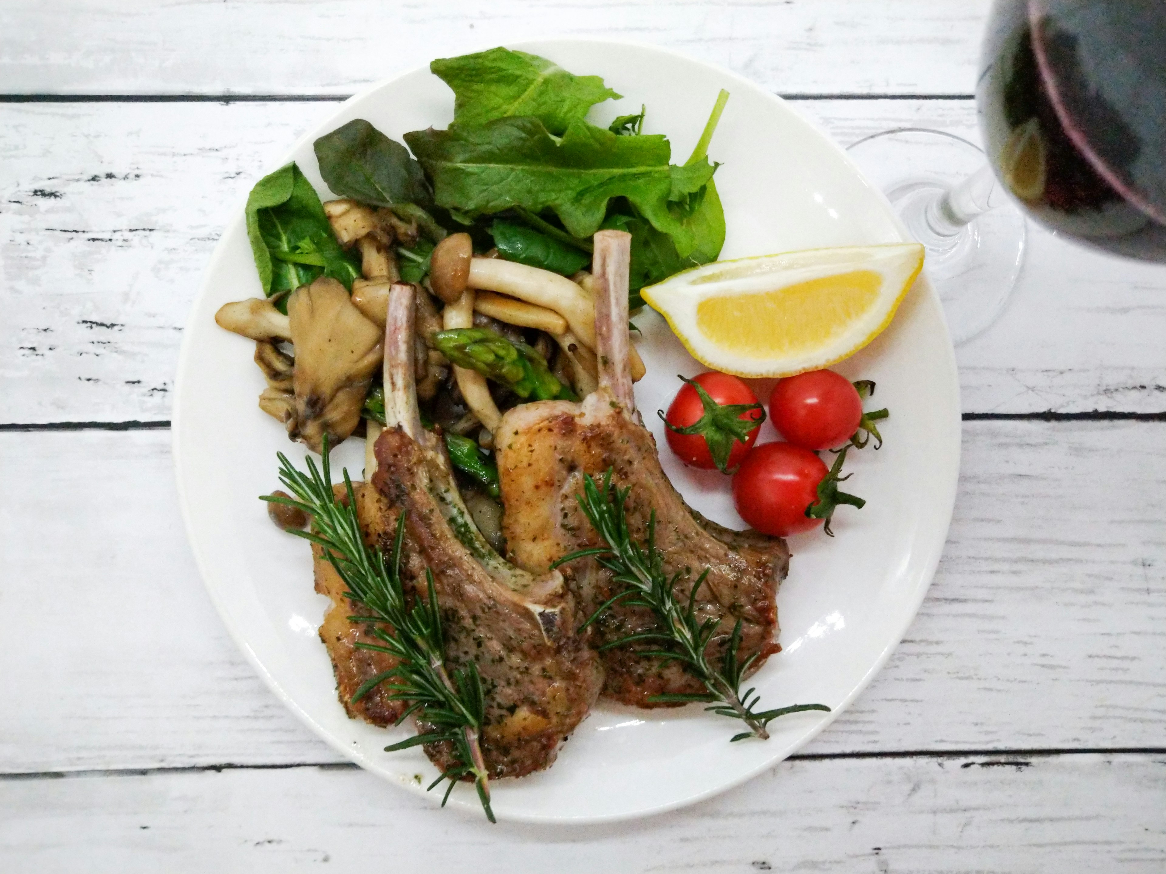 Delicious lamb chops garnished with herbs served on a plate with lemon and tomatoes alongside salad and mushrooms