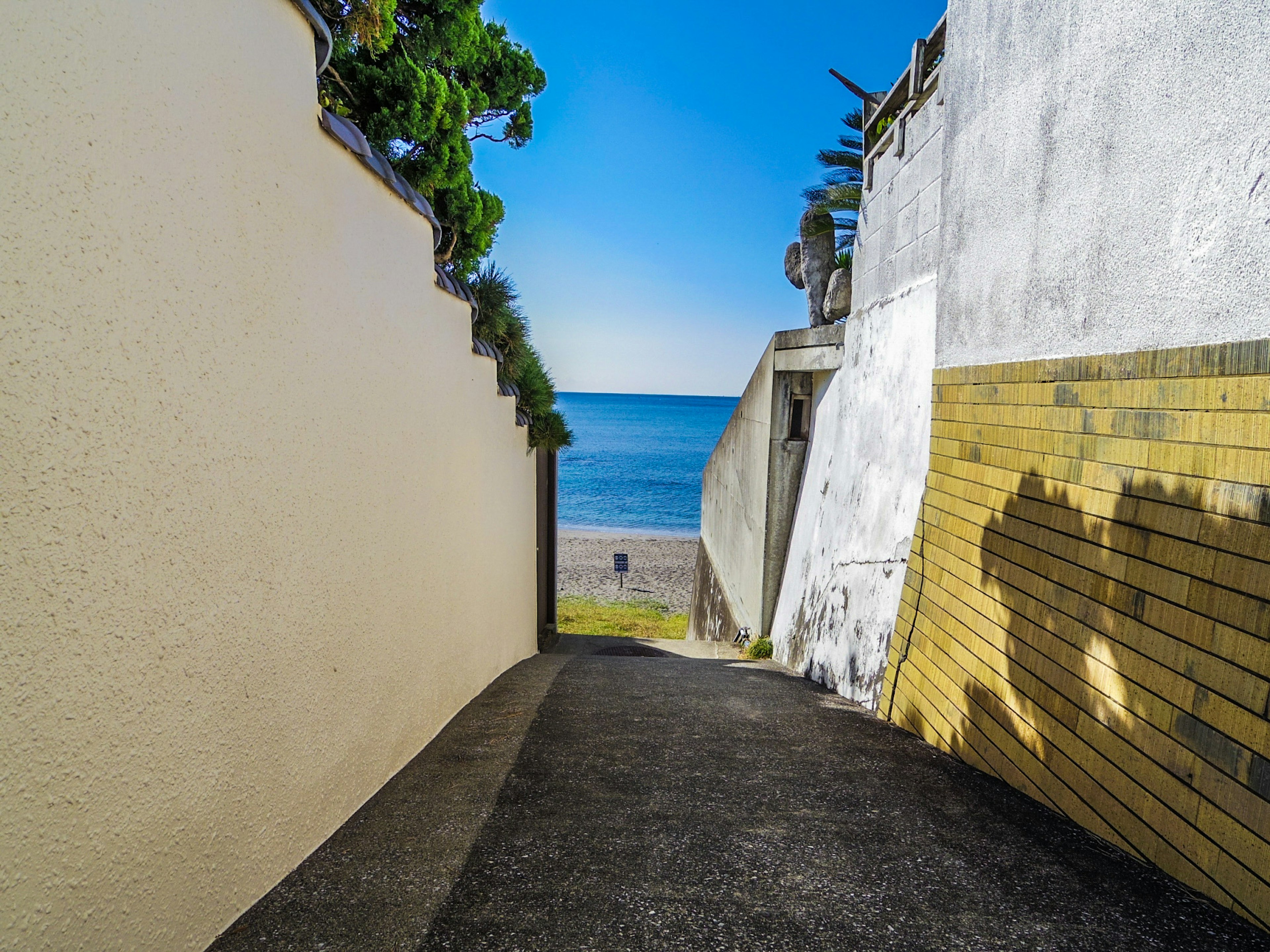 Ein Weg, der zum blauen Meer führt, umgeben von Wänden und Pflanzen