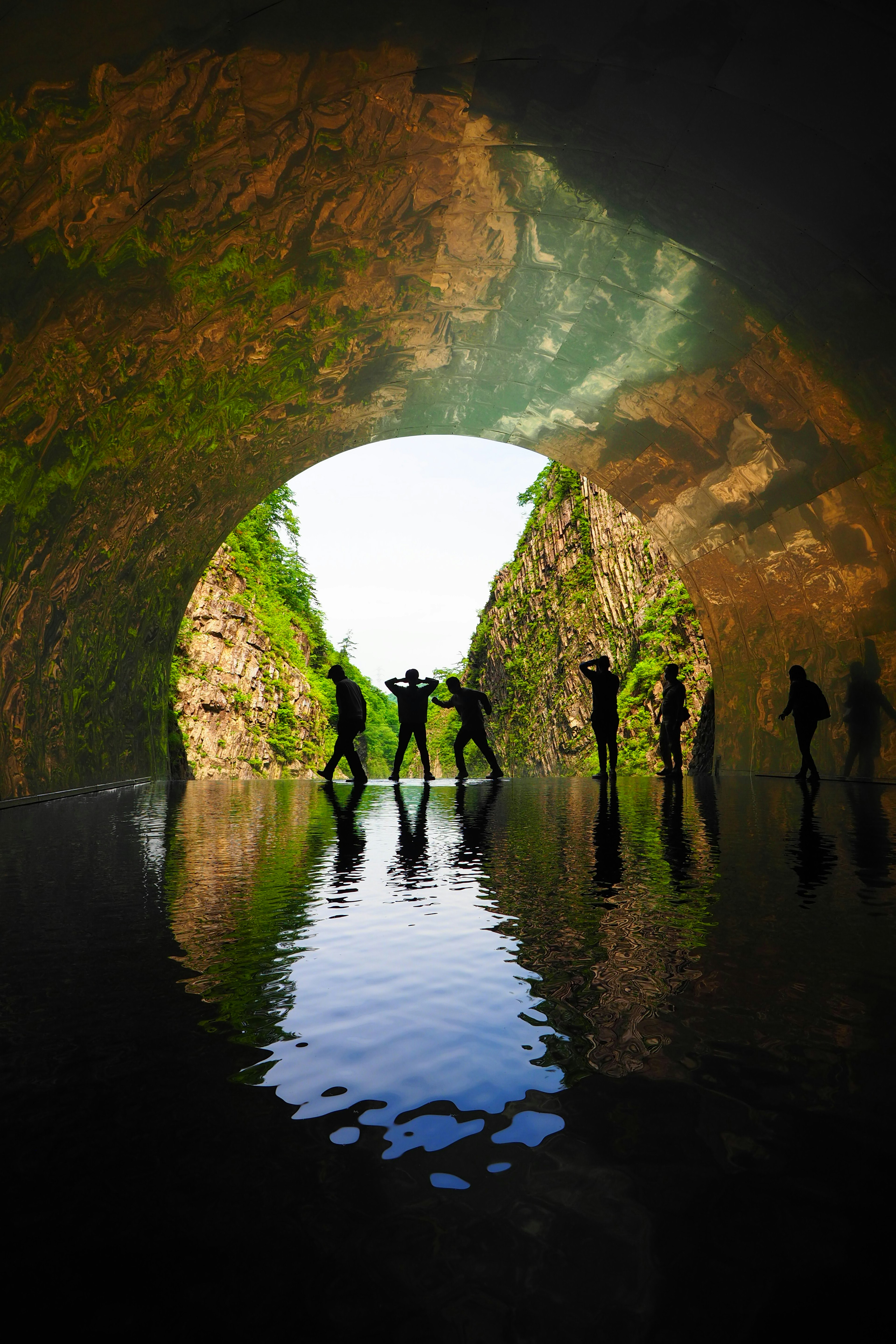 Silhouettes de personnes reflétées dans l'eau à l'intérieur d'un tunnel avec une végétation luxuriante