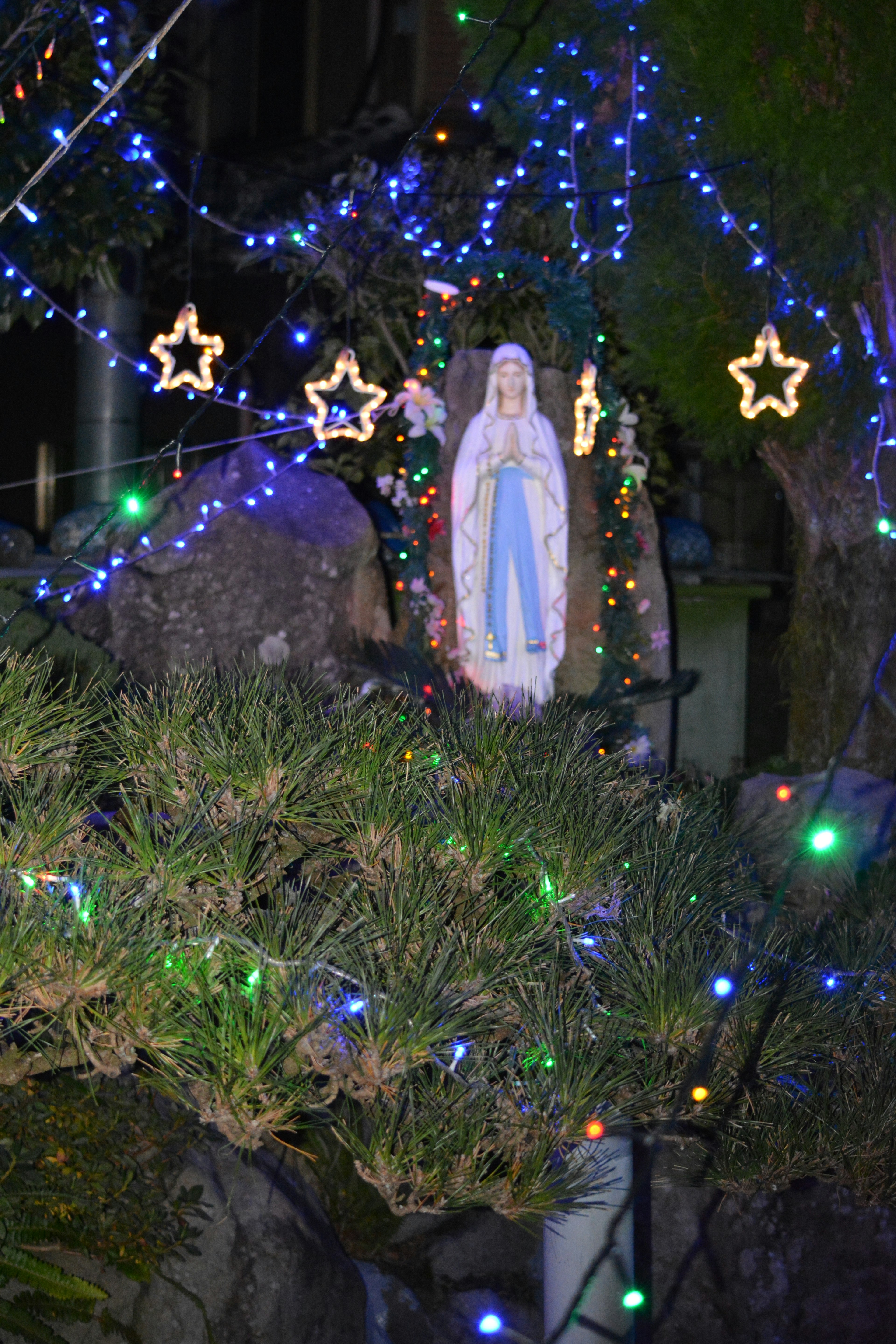 Scene featuring a statue of Virgin Mary surrounded by blue lights and star-shaped decorations