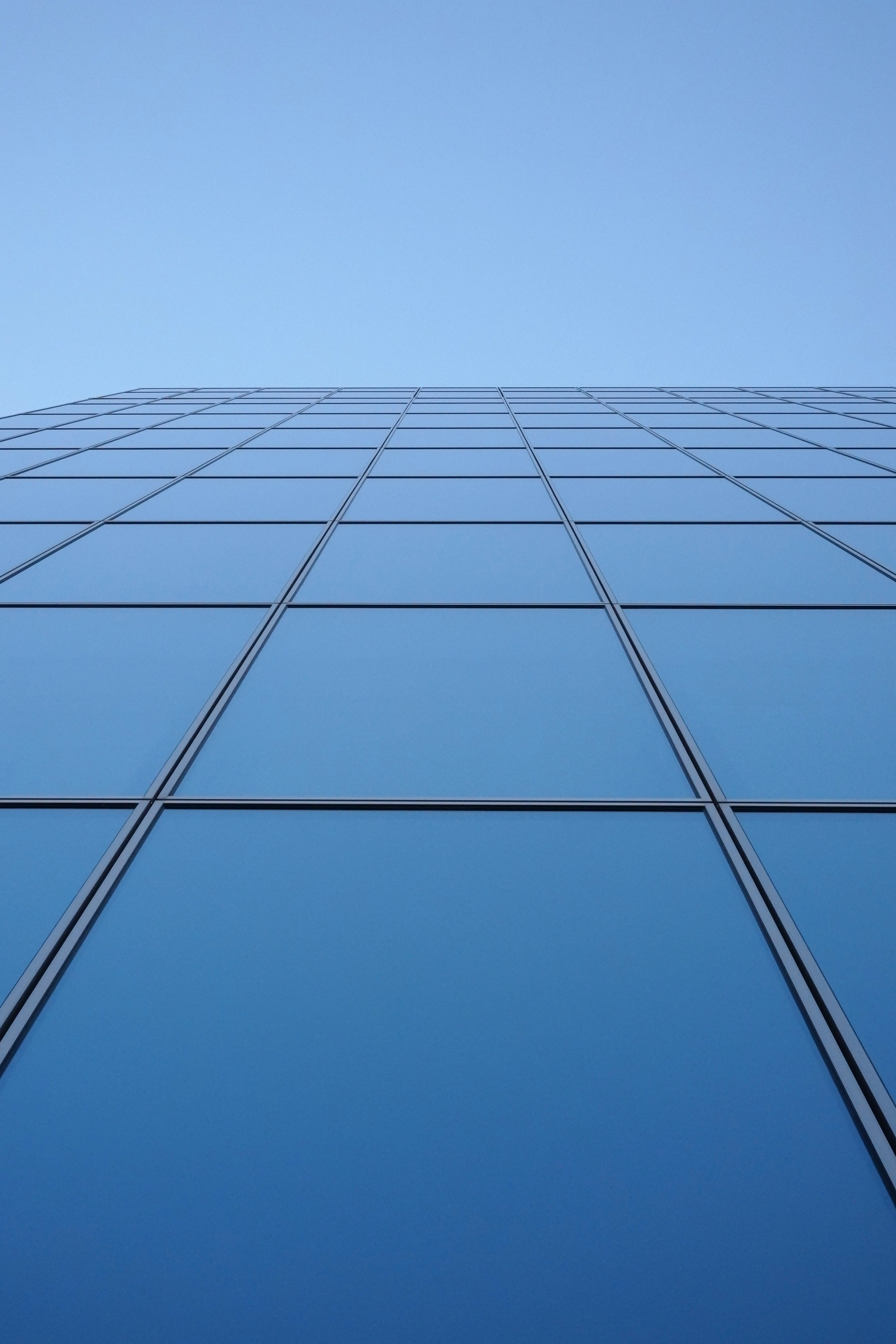 View of the upper section of a glass building against a blue sky