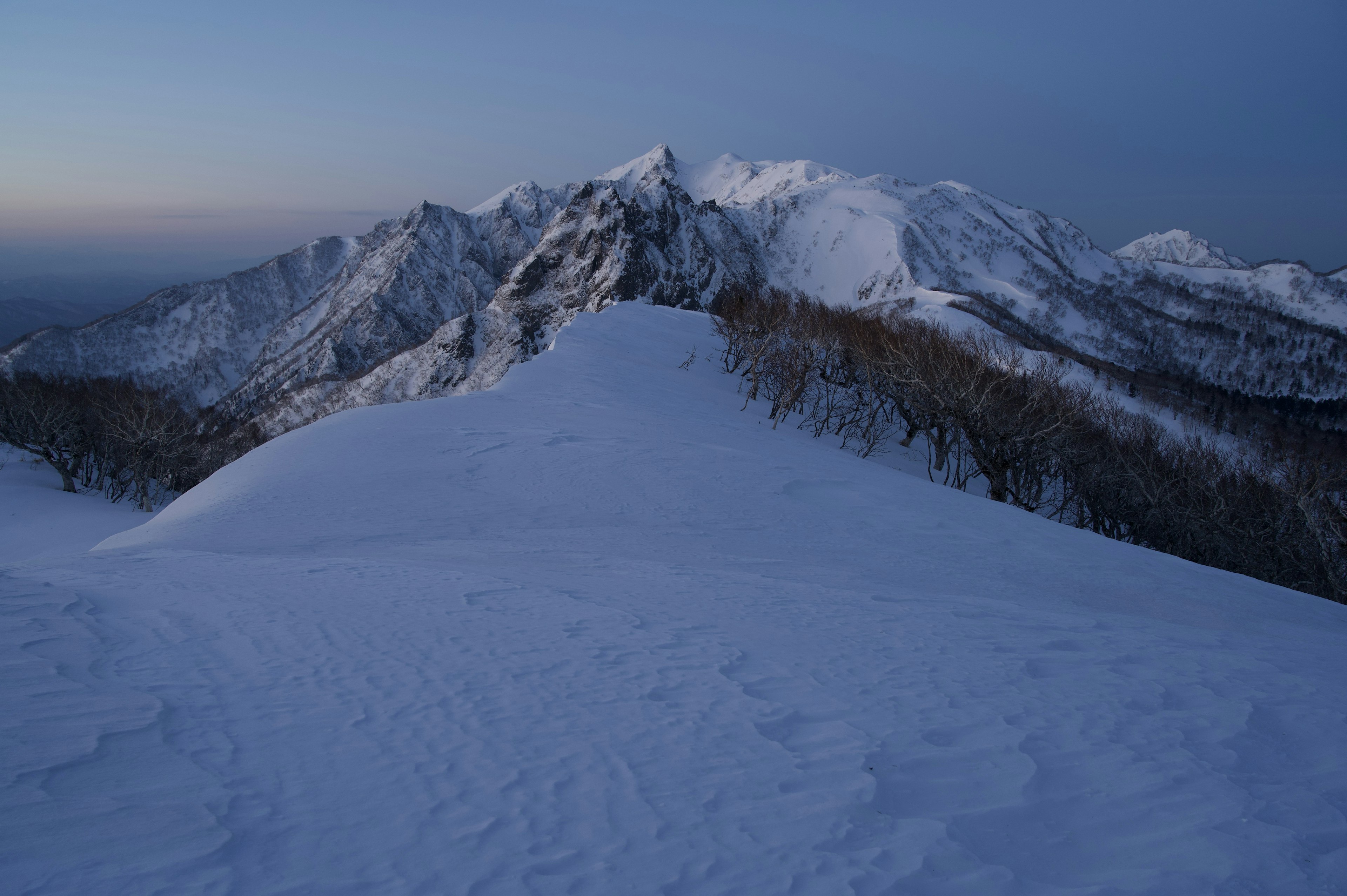 Paisaje de montañas cubiertas de nieve al atardecer con cielo azul y contraste de nieve