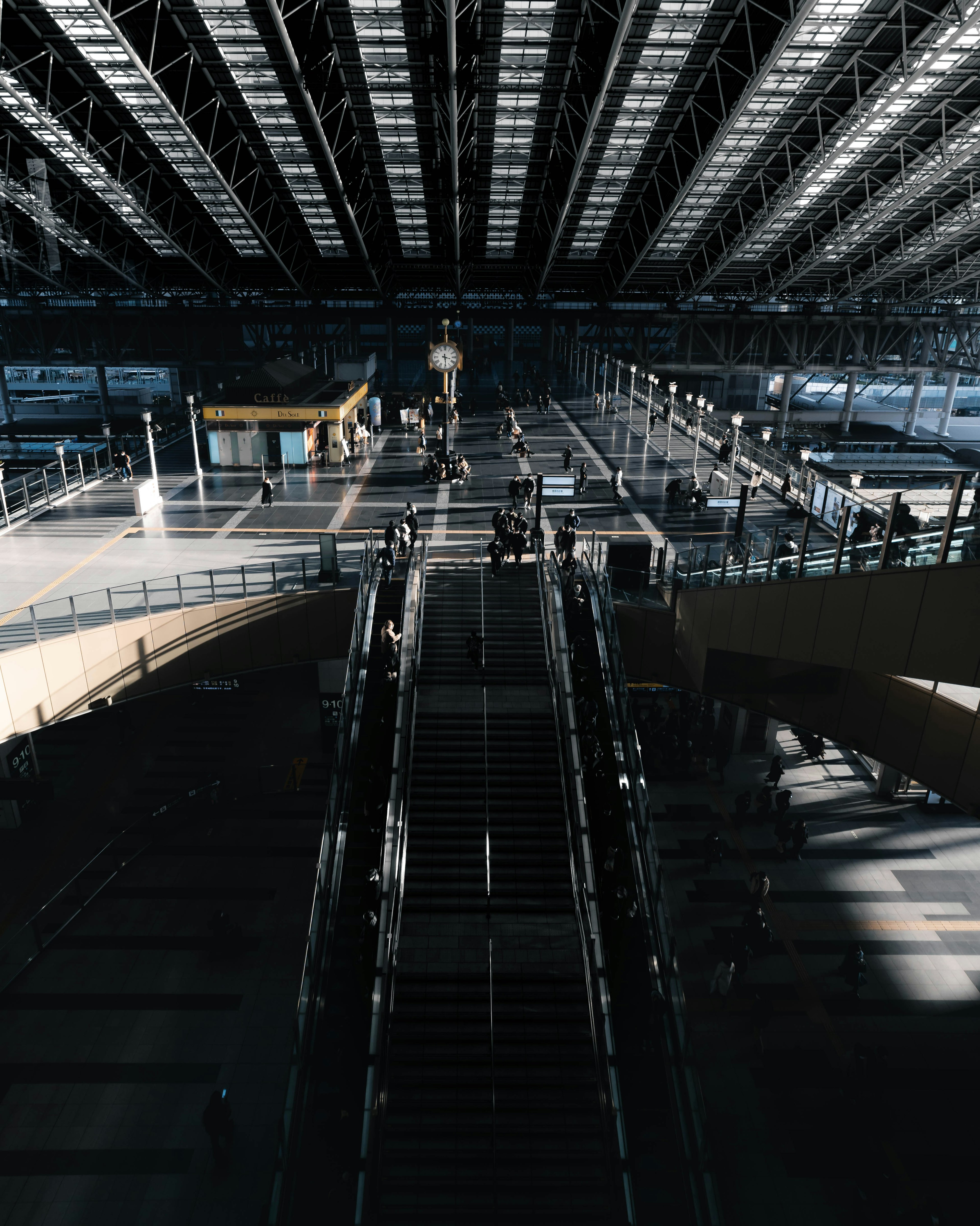 Interior view of a spacious train station with a large roof, visible stairs and platforms