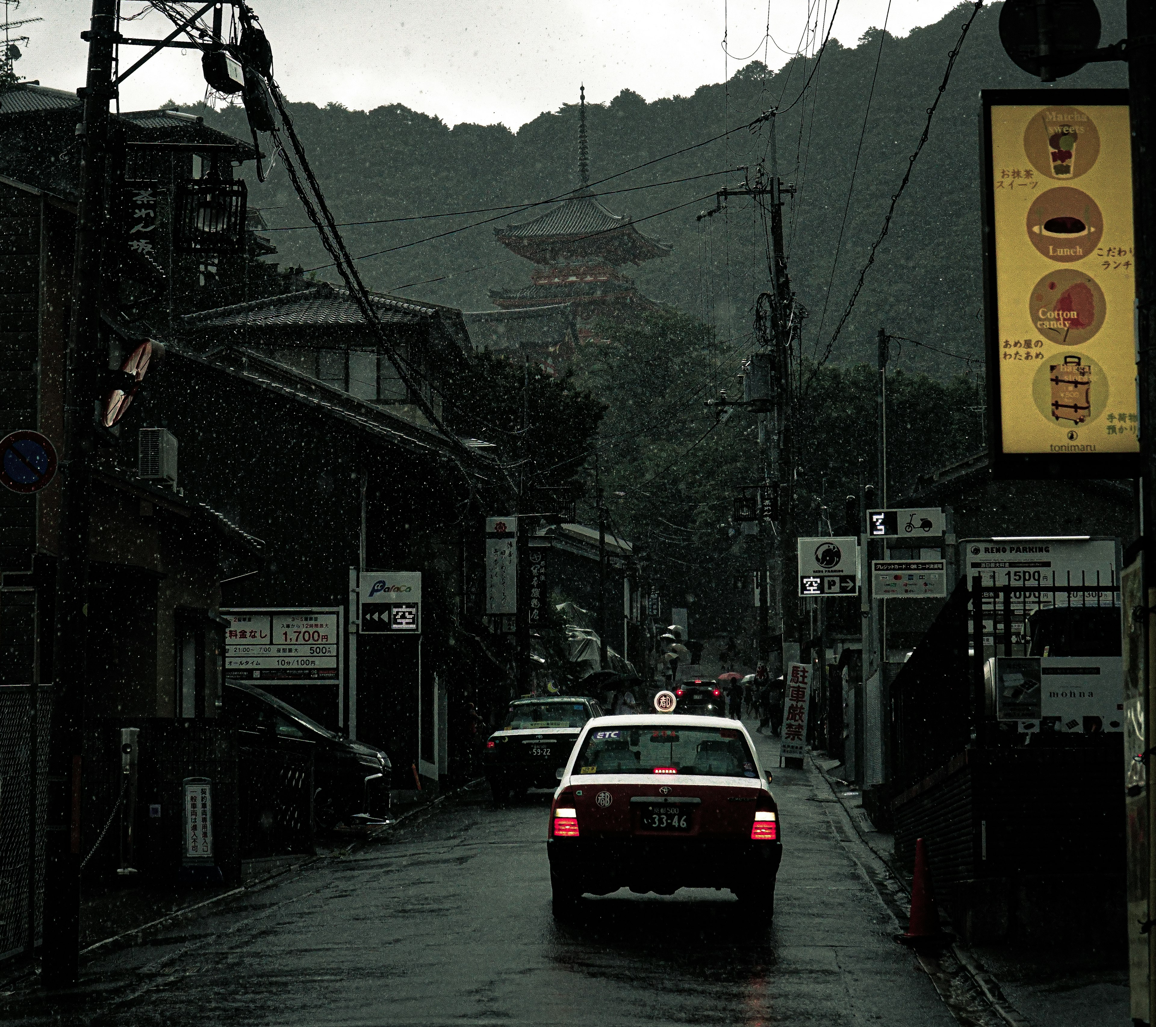 Scène de rue japonaise avec un taxi sous la pluie et des montagnes en arrière-plan