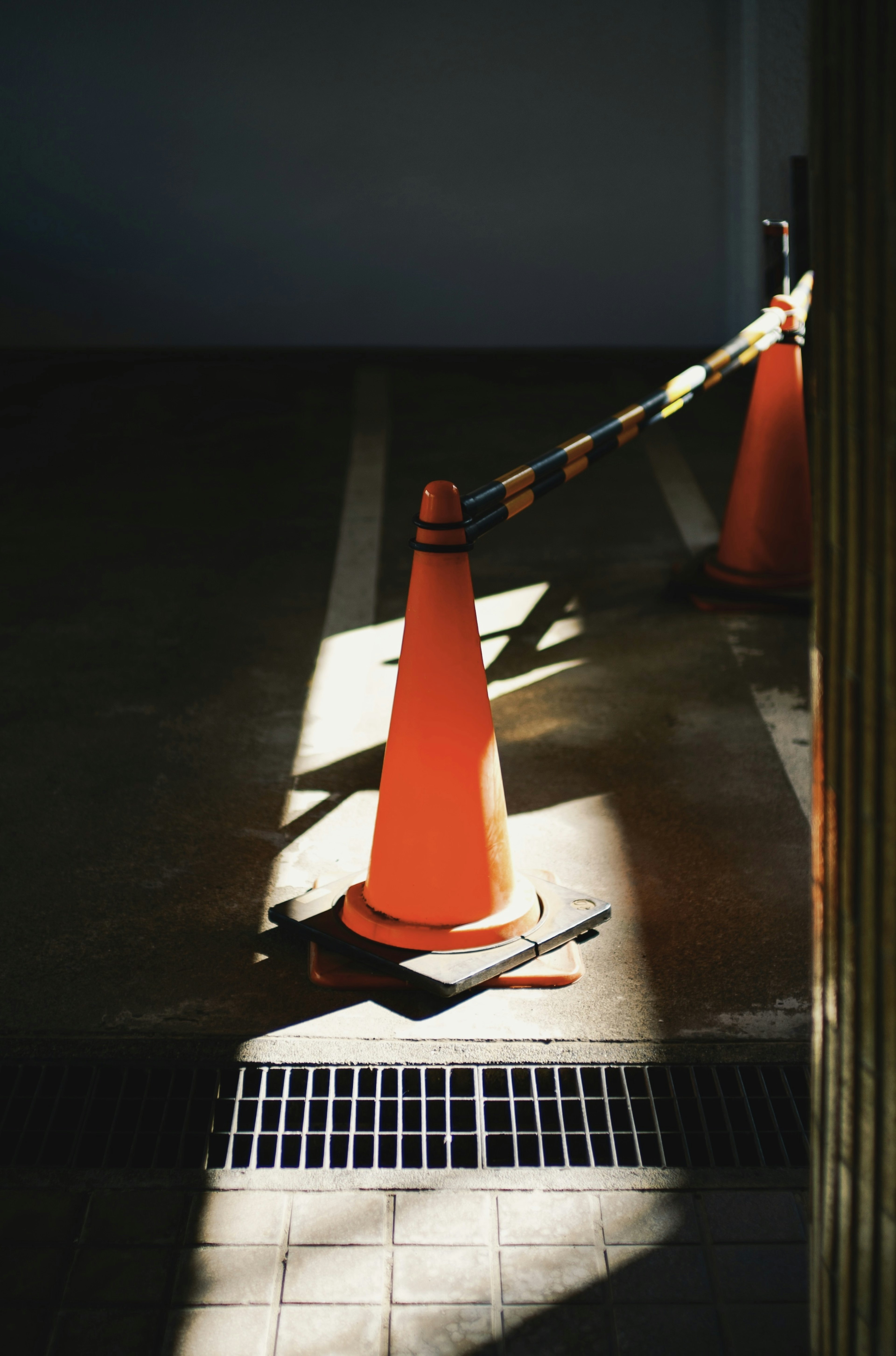 An orange traffic cone with caution tape in a dimly lit area