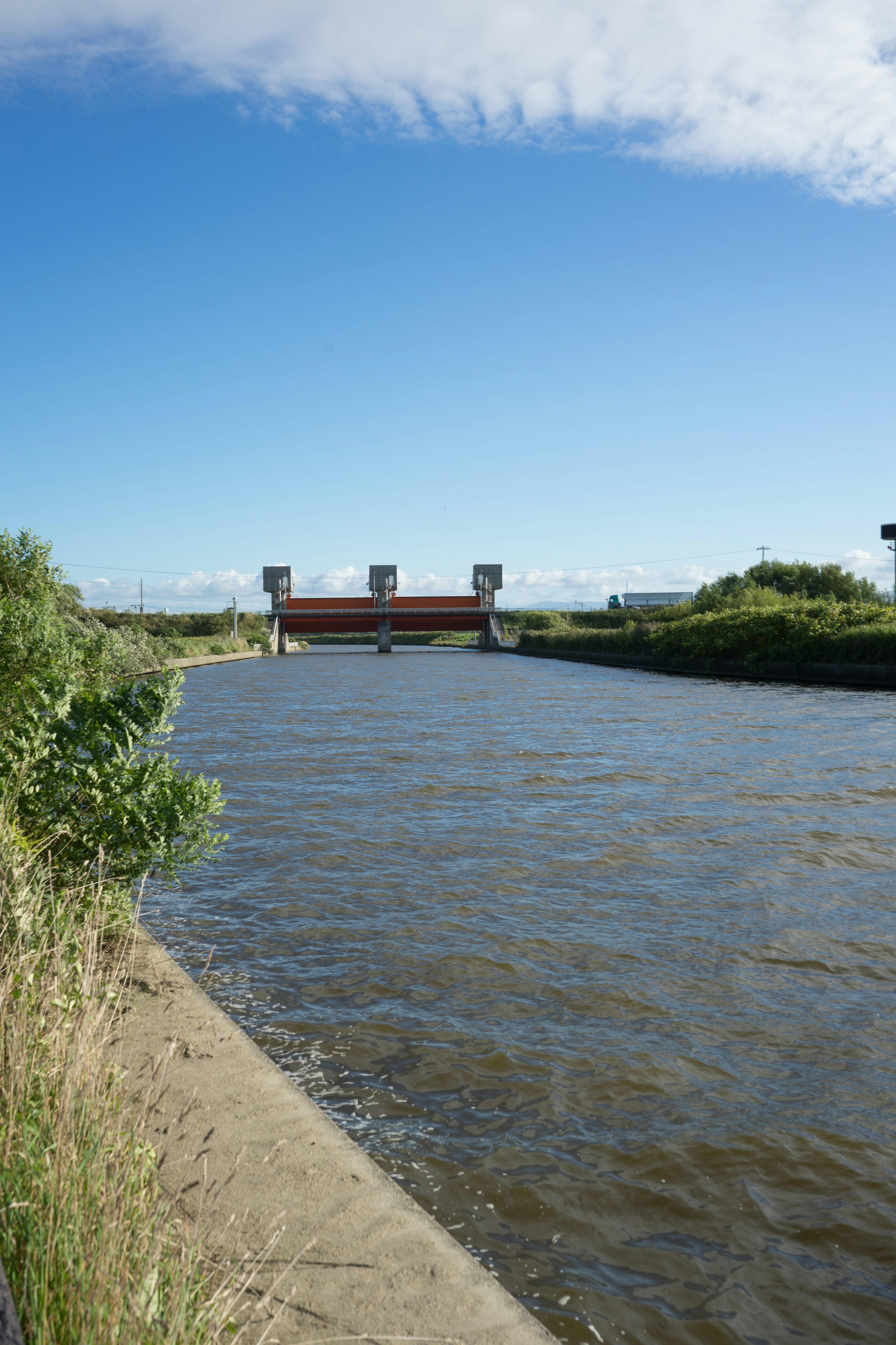 Fiume con struttura di diga sotto un cielo blu chiaro e vegetazione verde