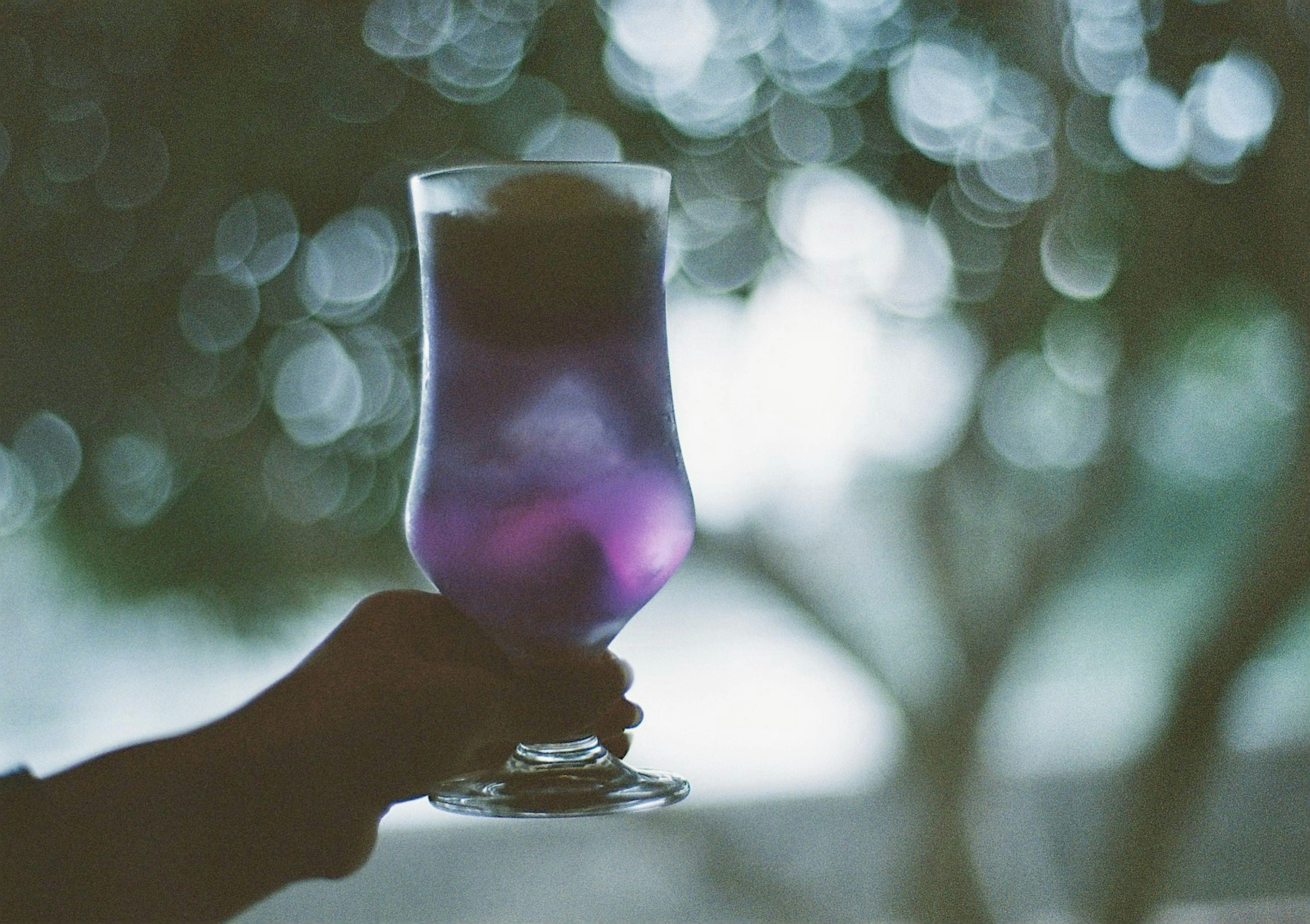 Purple cocktail glass held in hand with a blurred background