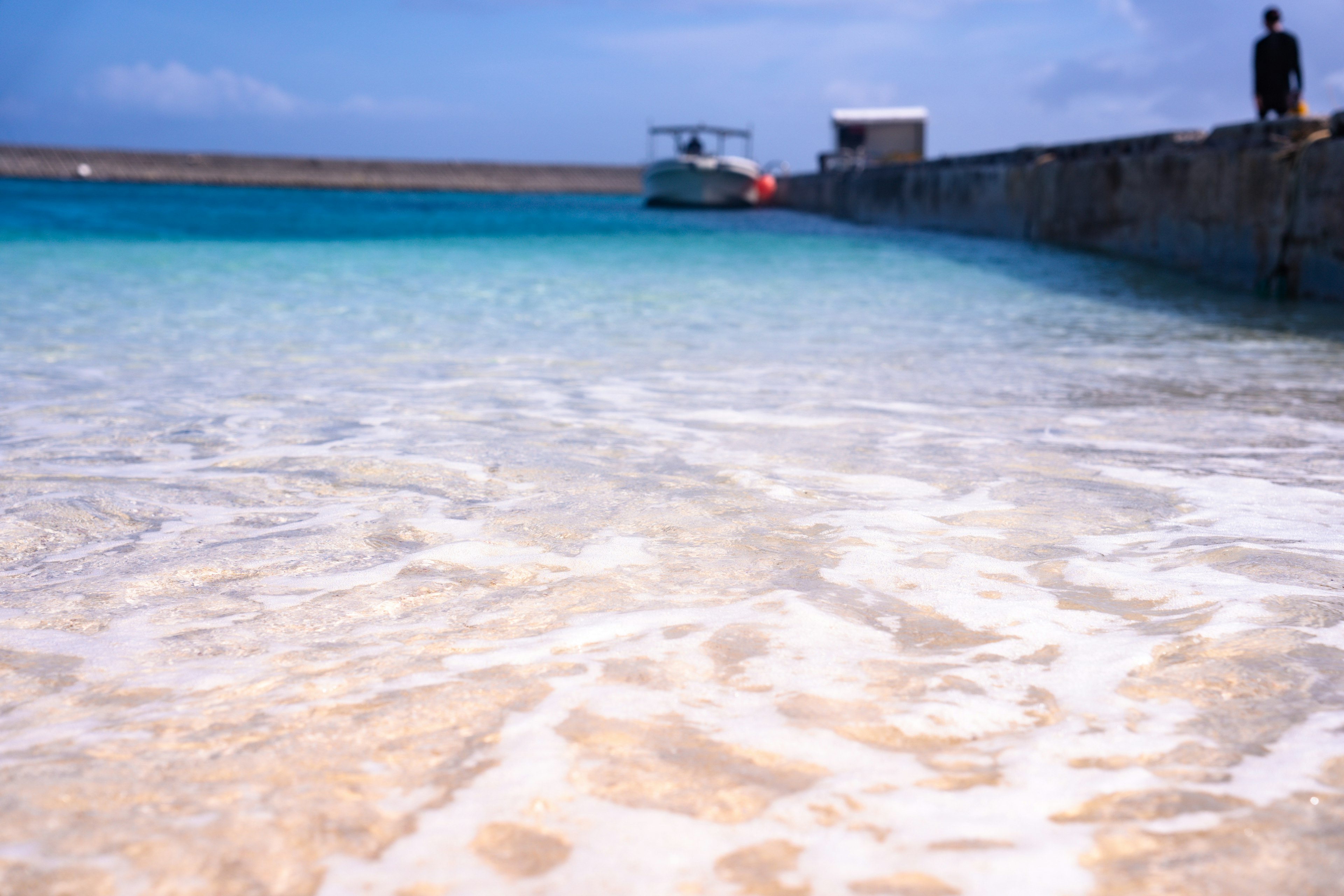 Clear blue sea with white sandy beach and a boat docked in the distance