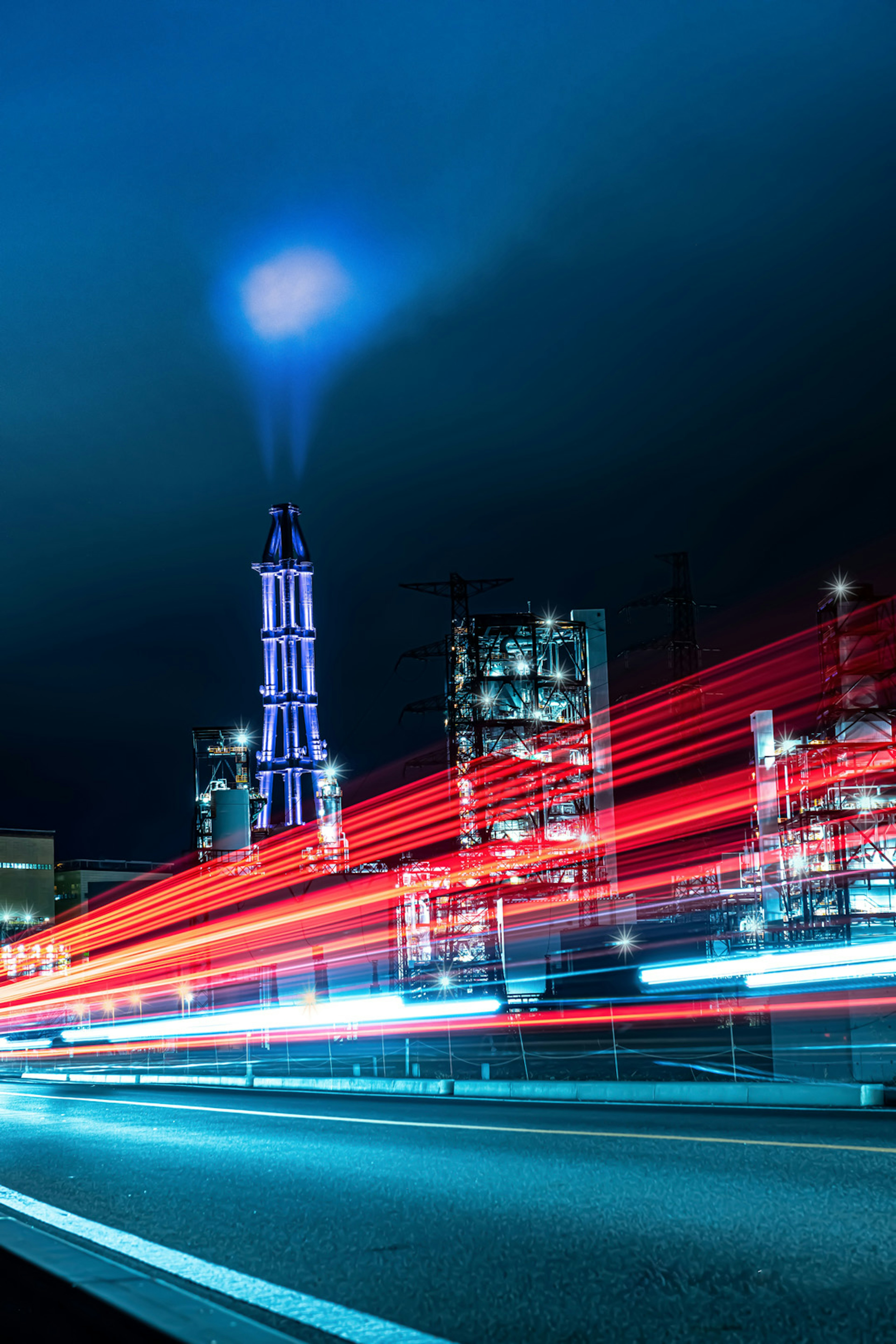 Factory smokestack illuminated at night with light trails from passing vehicles