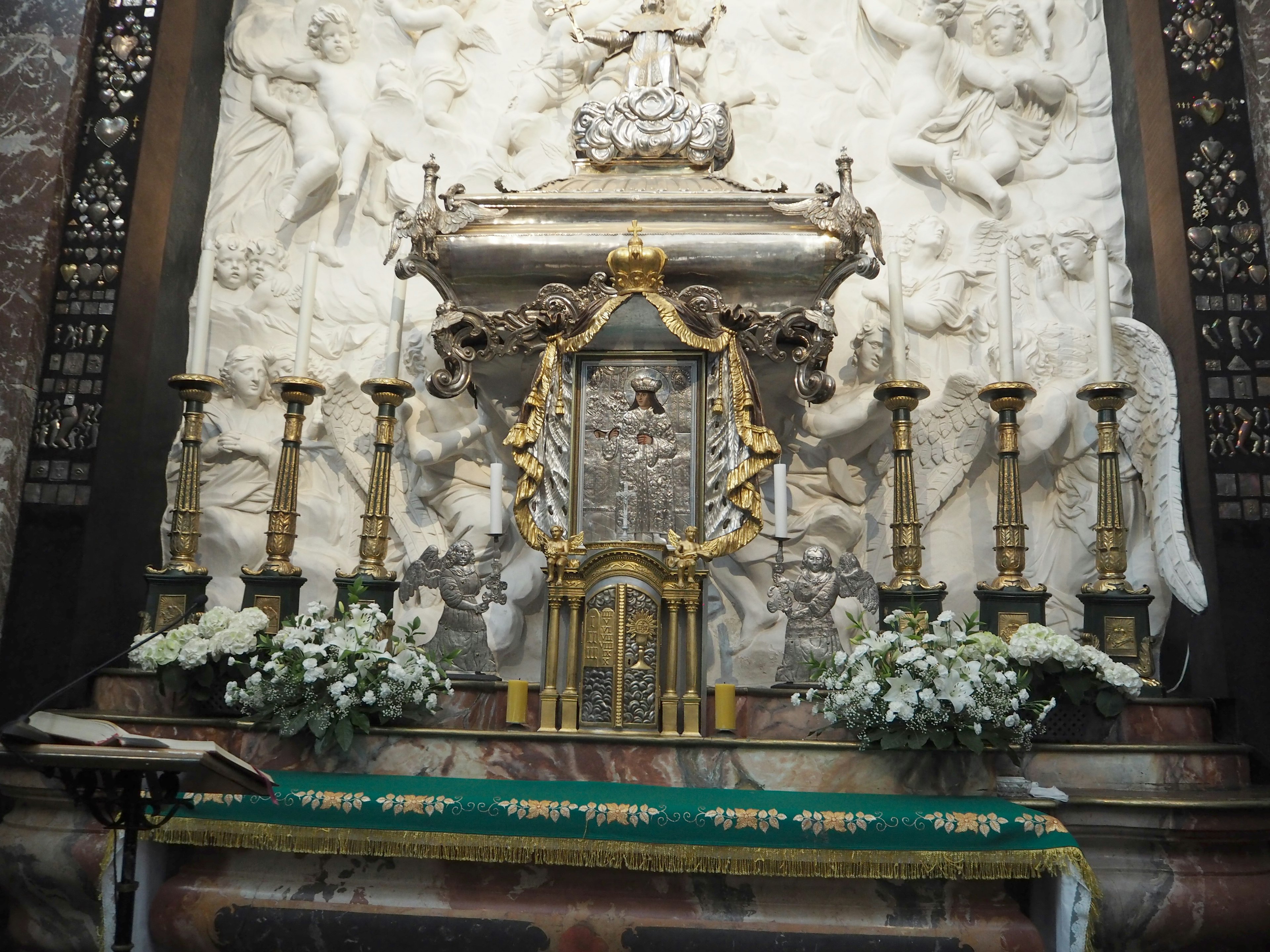 Autel orné avec des décorations dorées et des arrangements floraux blancs sur un fond sculpté en pierre