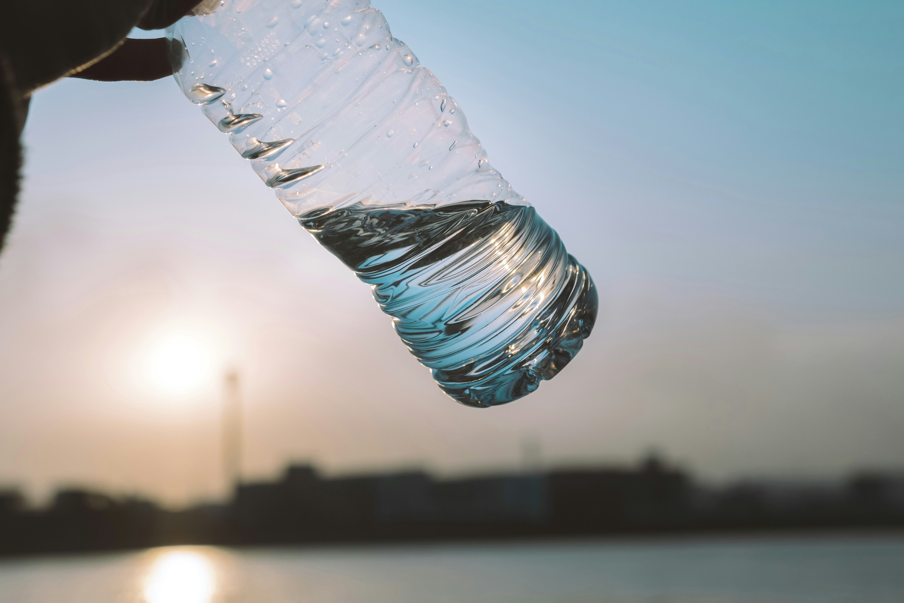 A hand holding a water bottle with a sunset in the background