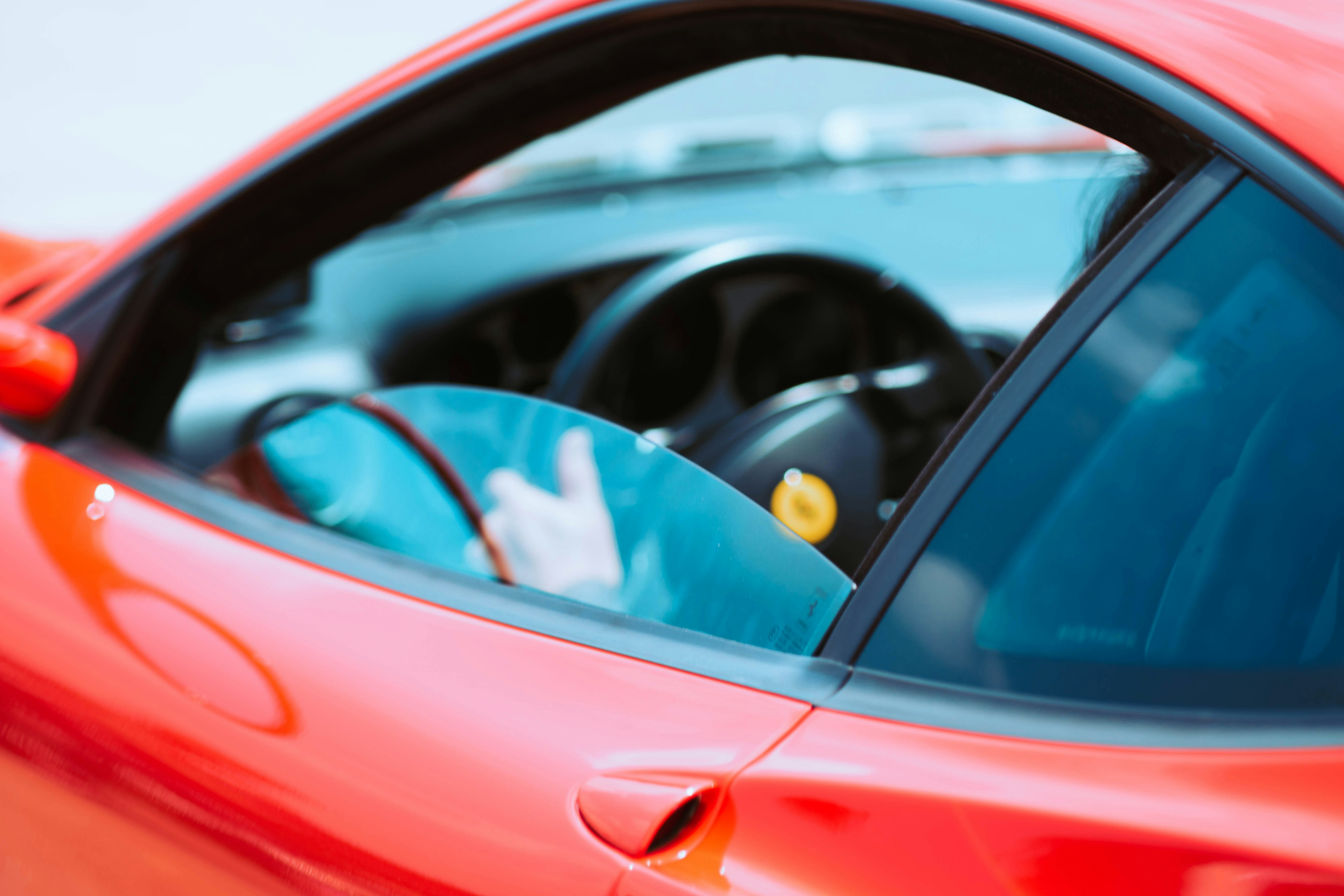 Vista interna di una macchina sportiva rossa che mostra il volante e parte della porta