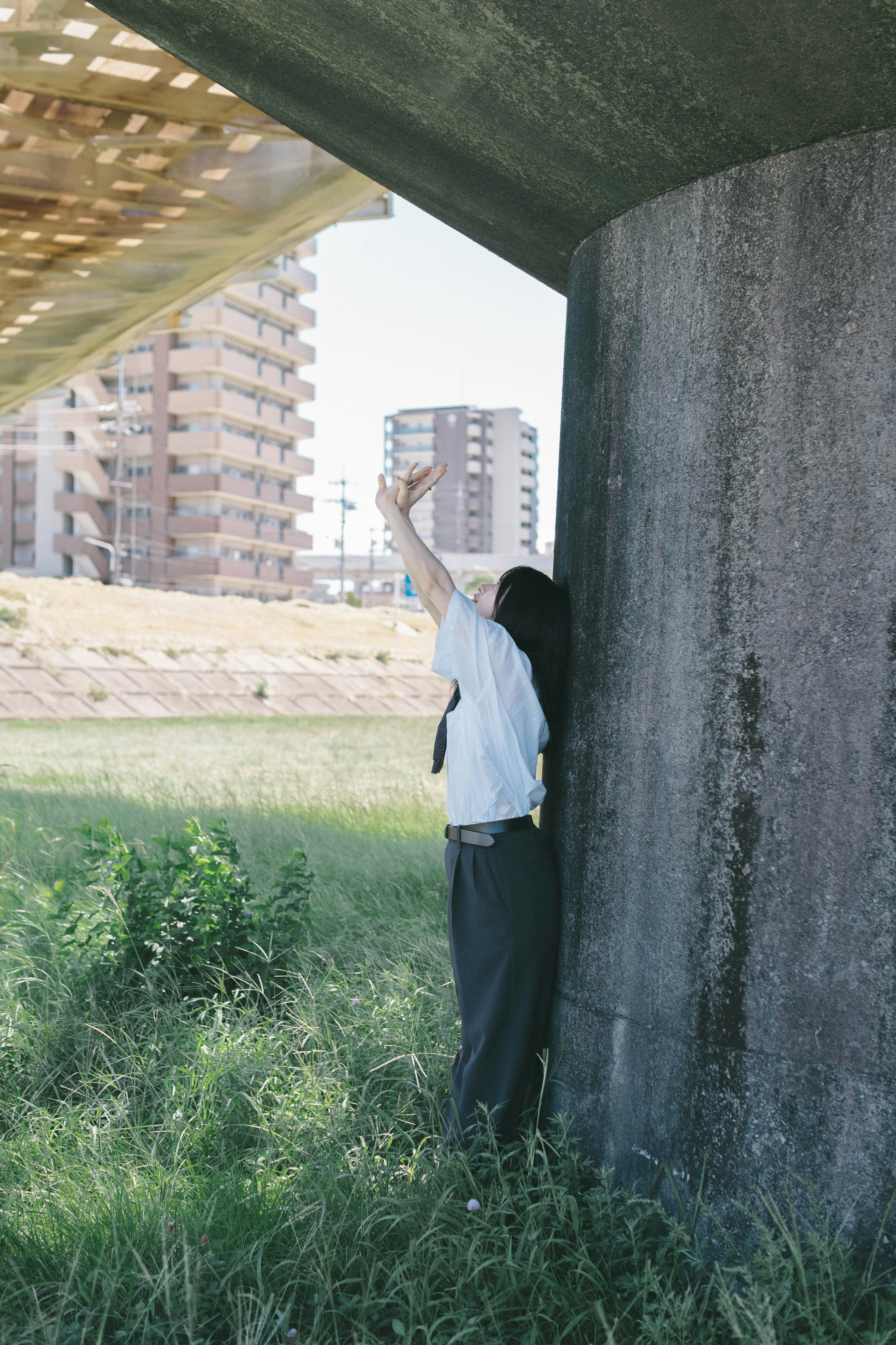 Persona levantando la mano debajo de un puente con edificios altos al fondo