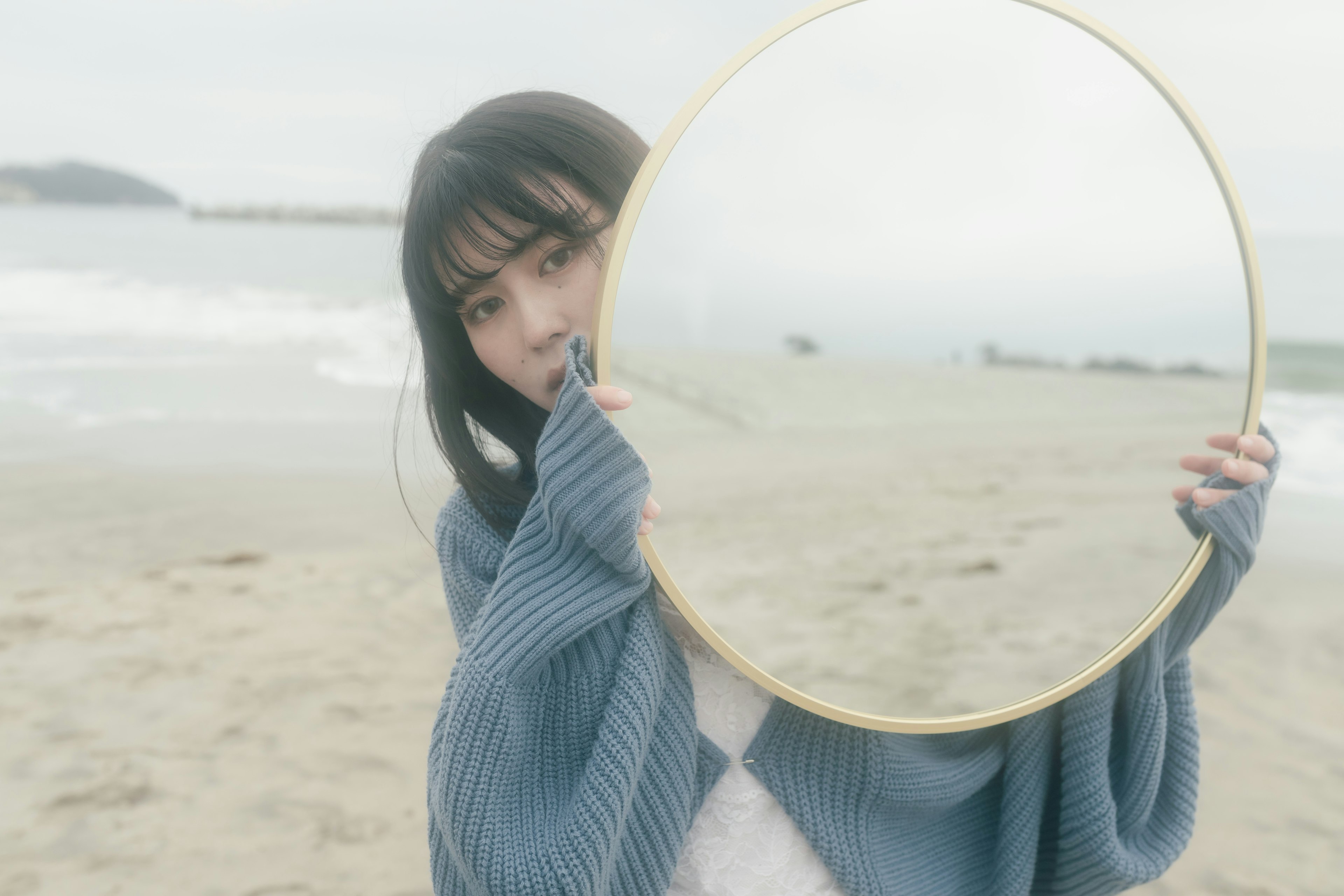 海辺で鏡を持つ女性のポートレート 濁った空と波が背景