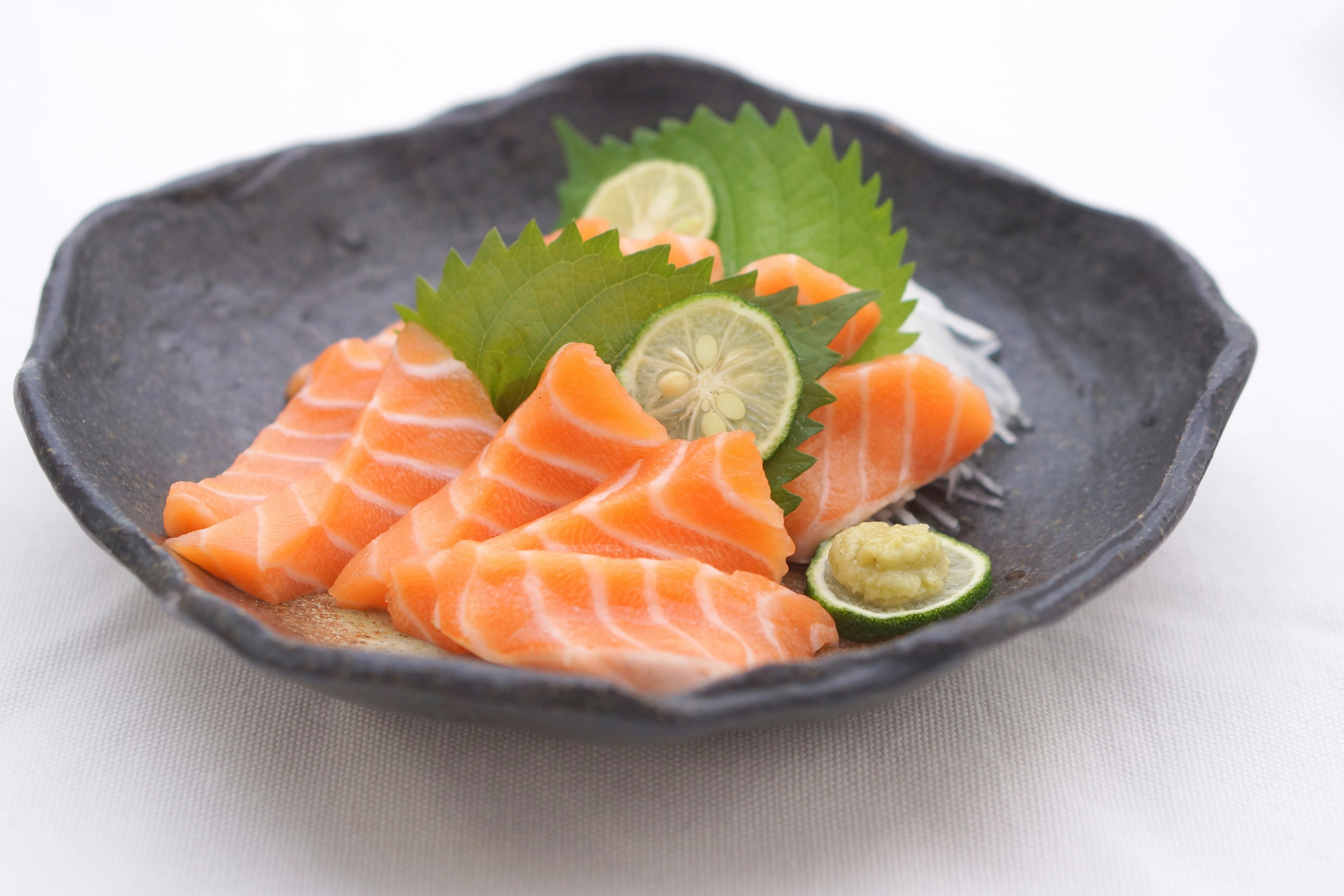 Sashimi salmon segar disusun di piring hitam dengan jeruk nipis dan wasabi