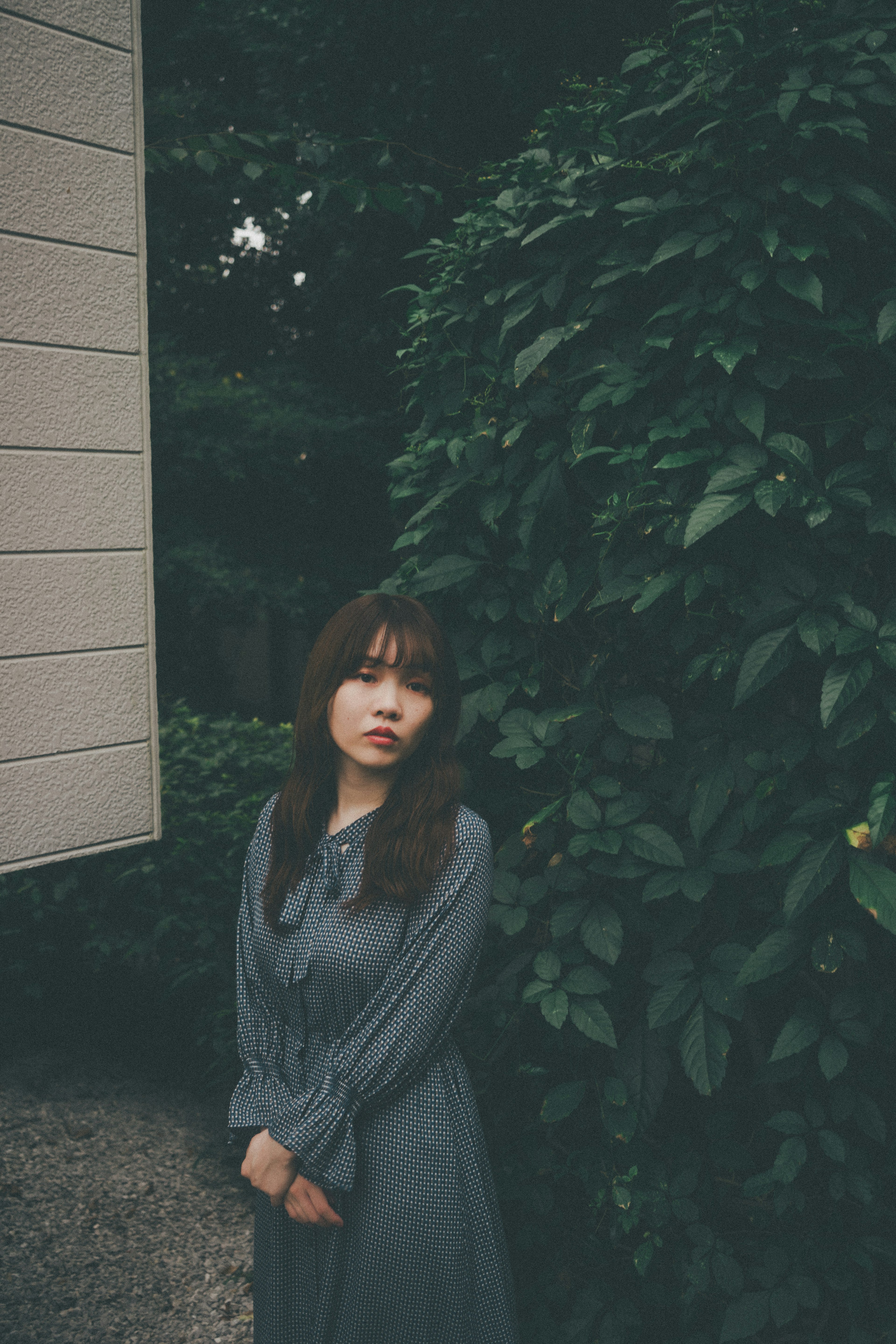 Portrait of a woman standing in front of green leaves wearing a gray dress