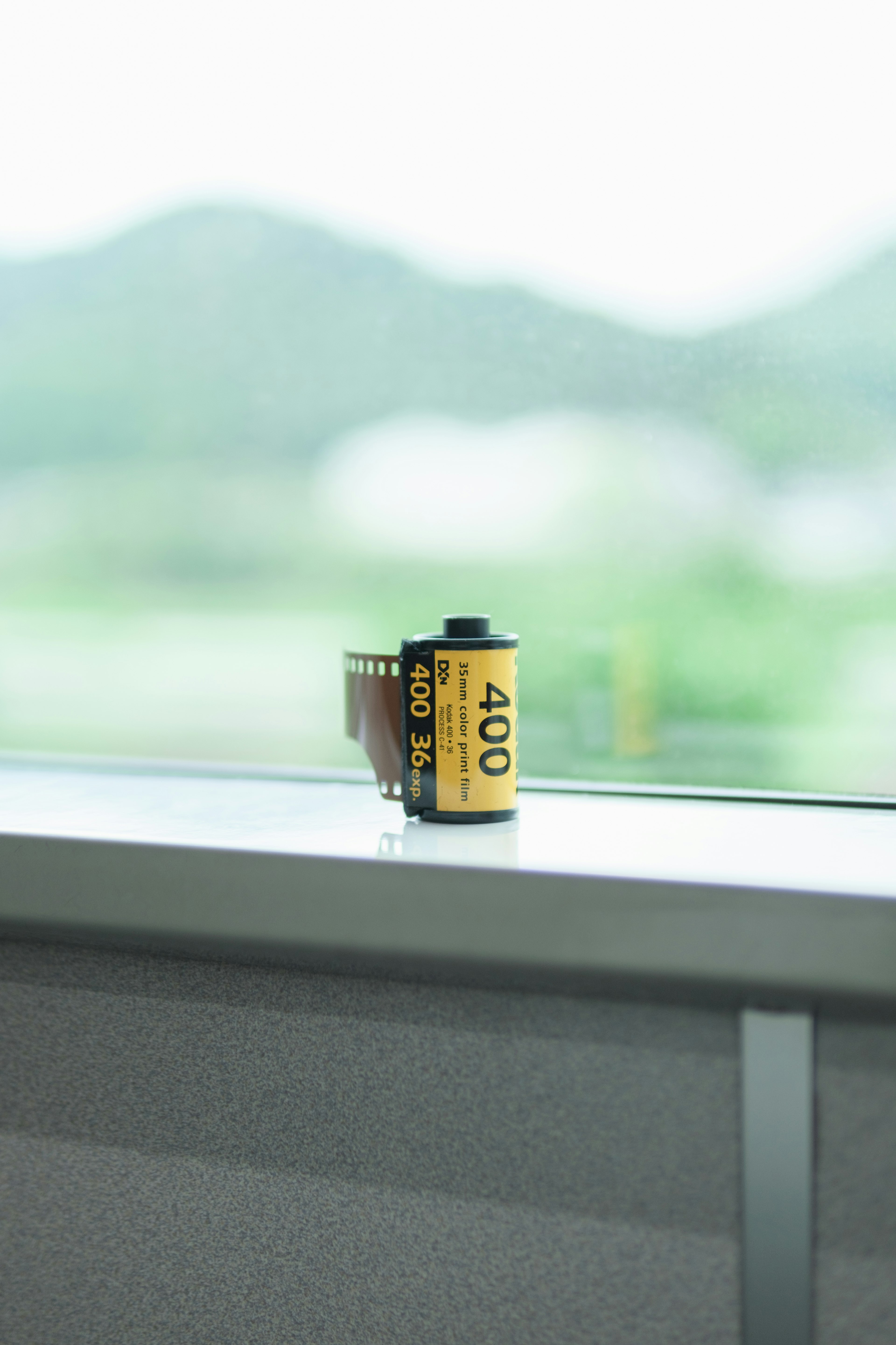 A roll of 400 film placed on a windowsill with blurred mountains in the background