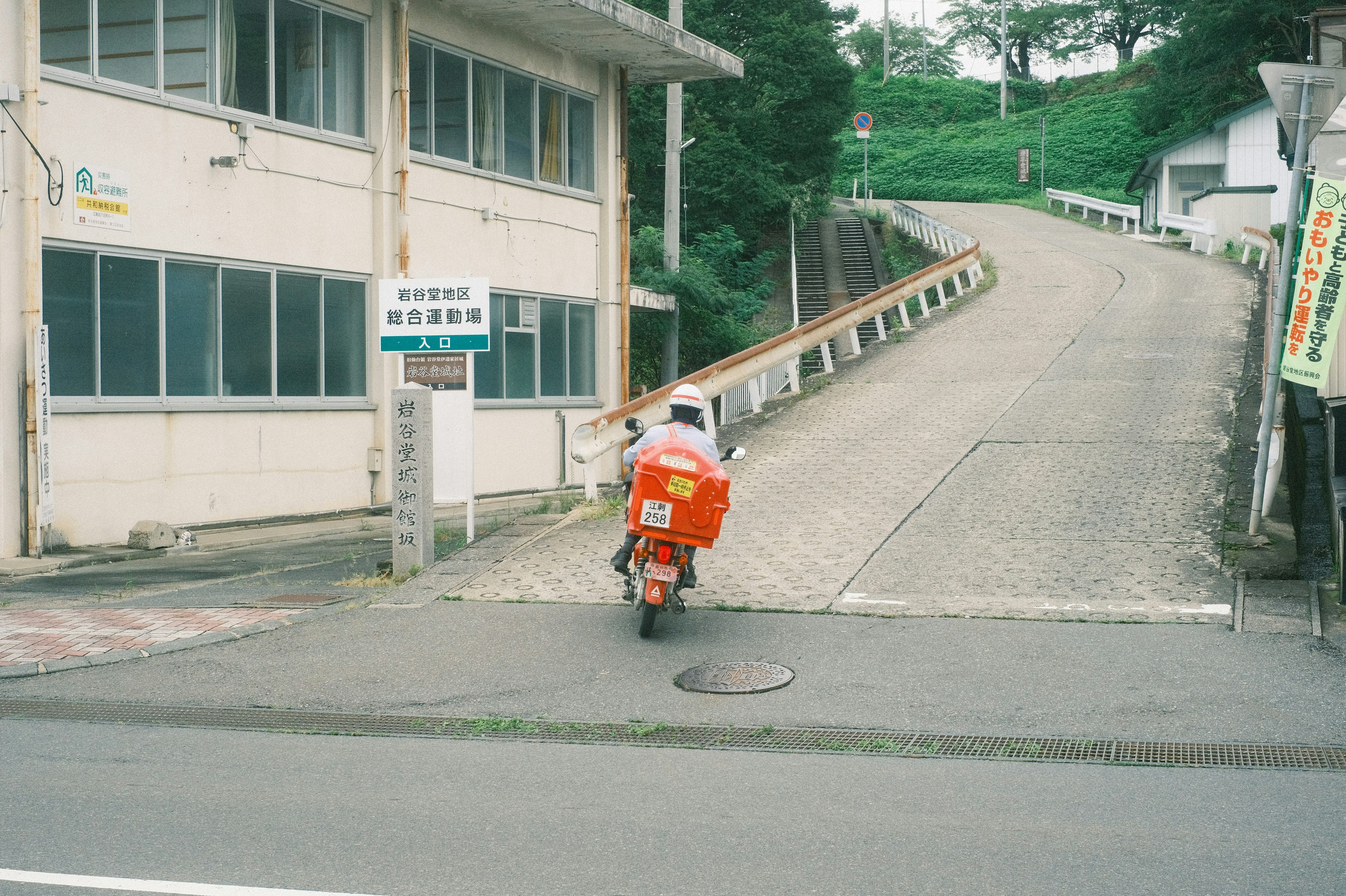 橙色摩托車在坡道上行駛，周圍有建築