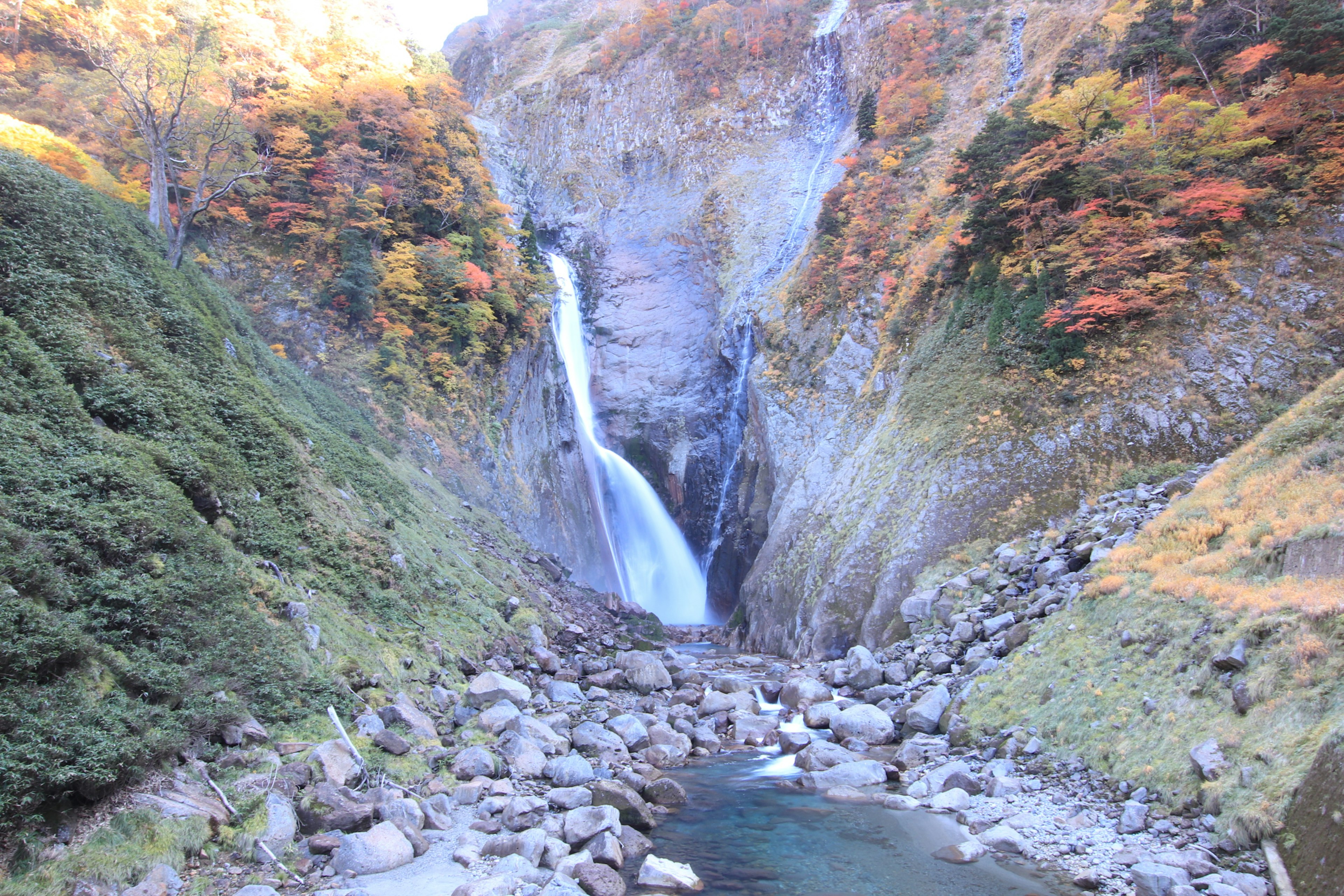 Malerischer Wasserfall umgeben von herbstlichem Laub und felsigem Gelände