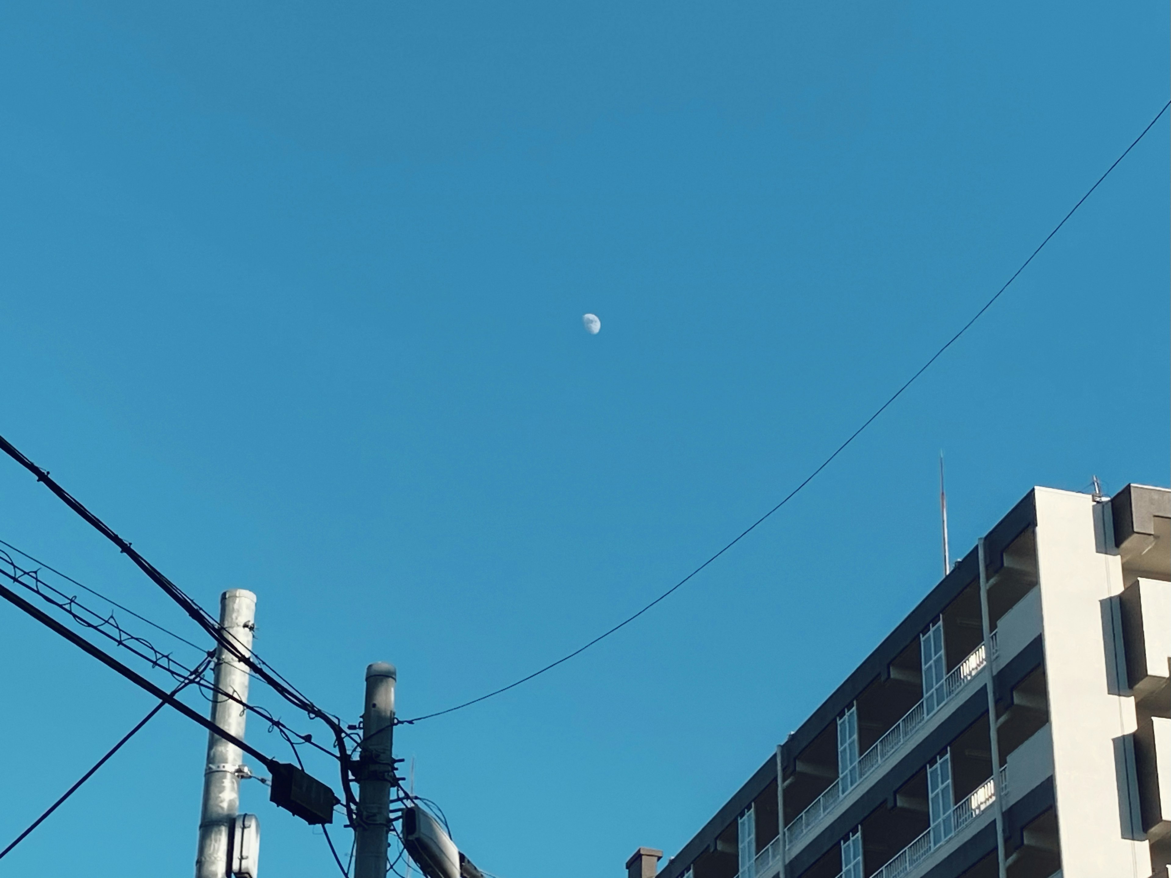 Mond im blauen Himmel über einem Gebäude und Stromleitungen