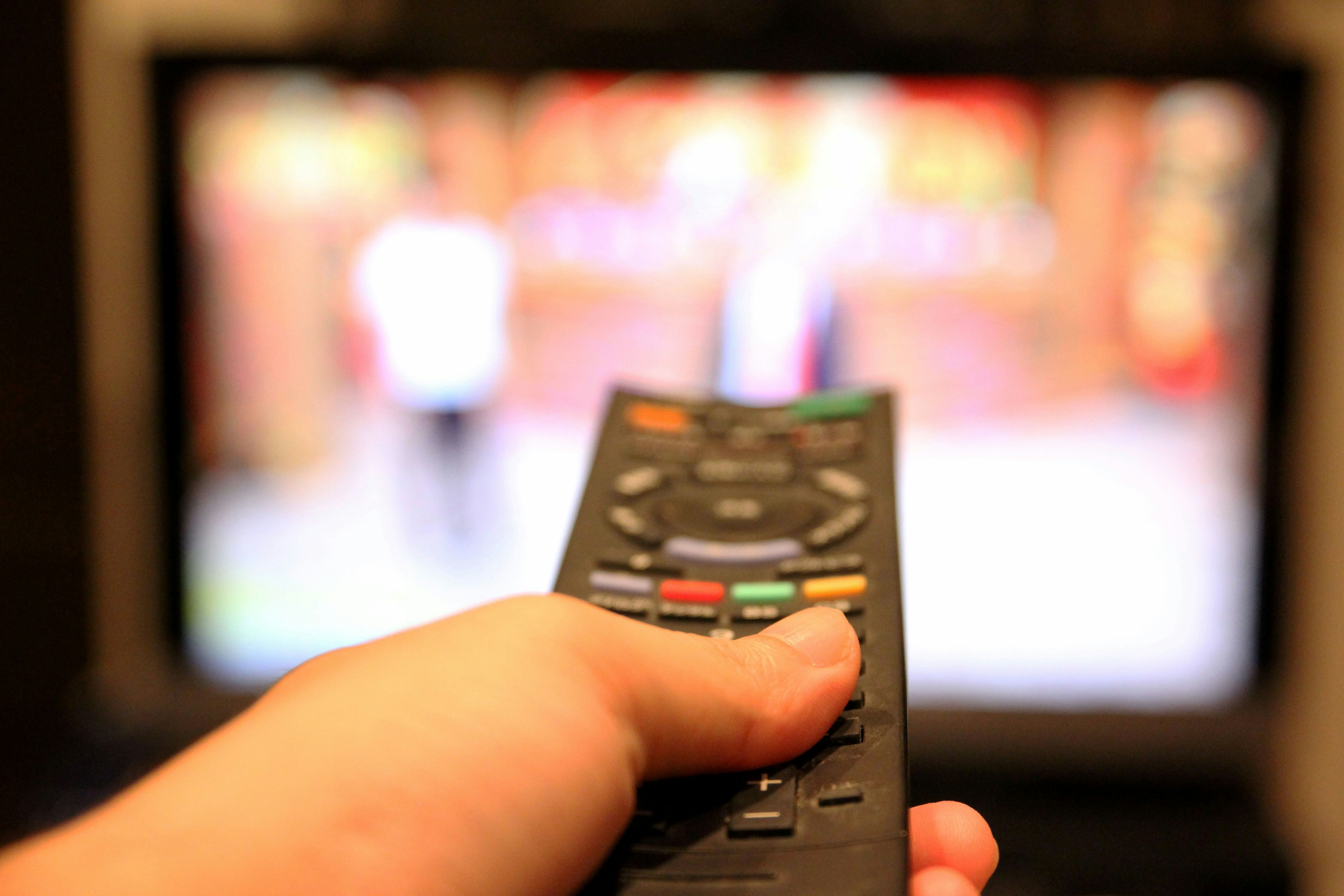 Tangan memegang remote control yang mengarah ke layar televisi