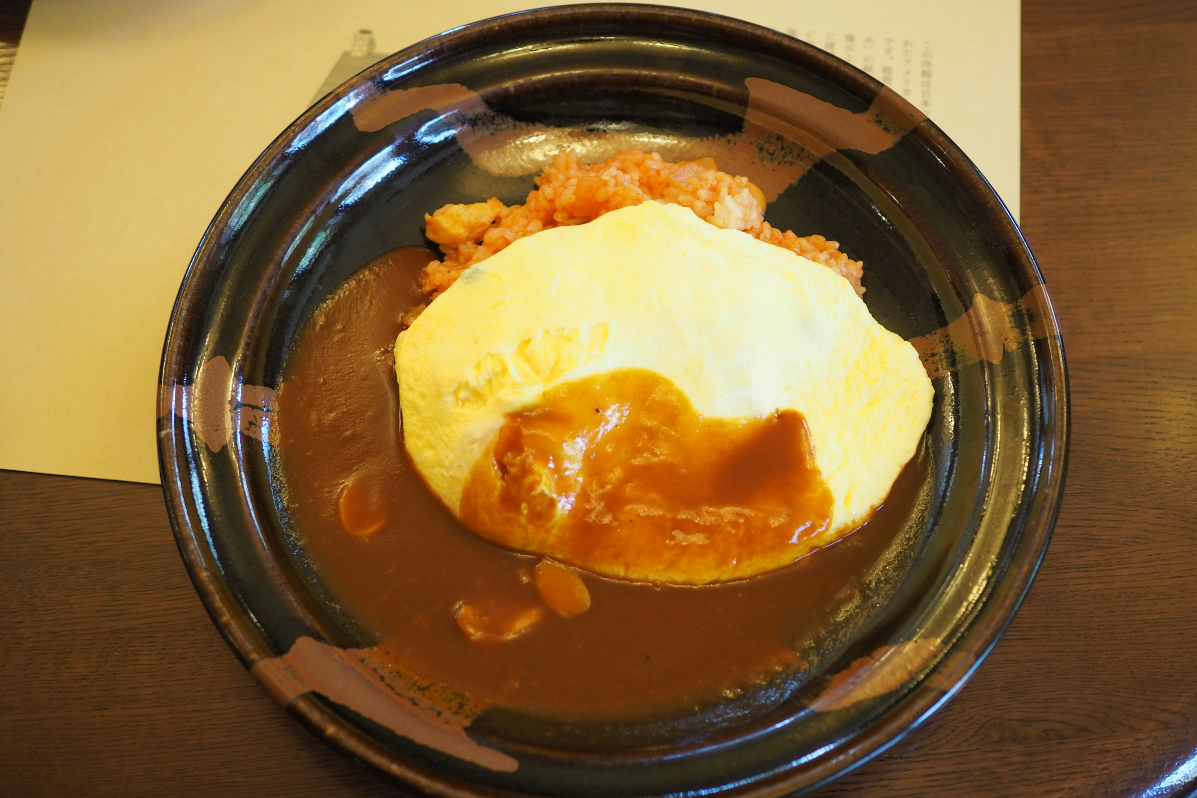 Omelette rice served on a black plate with demi-glace sauce