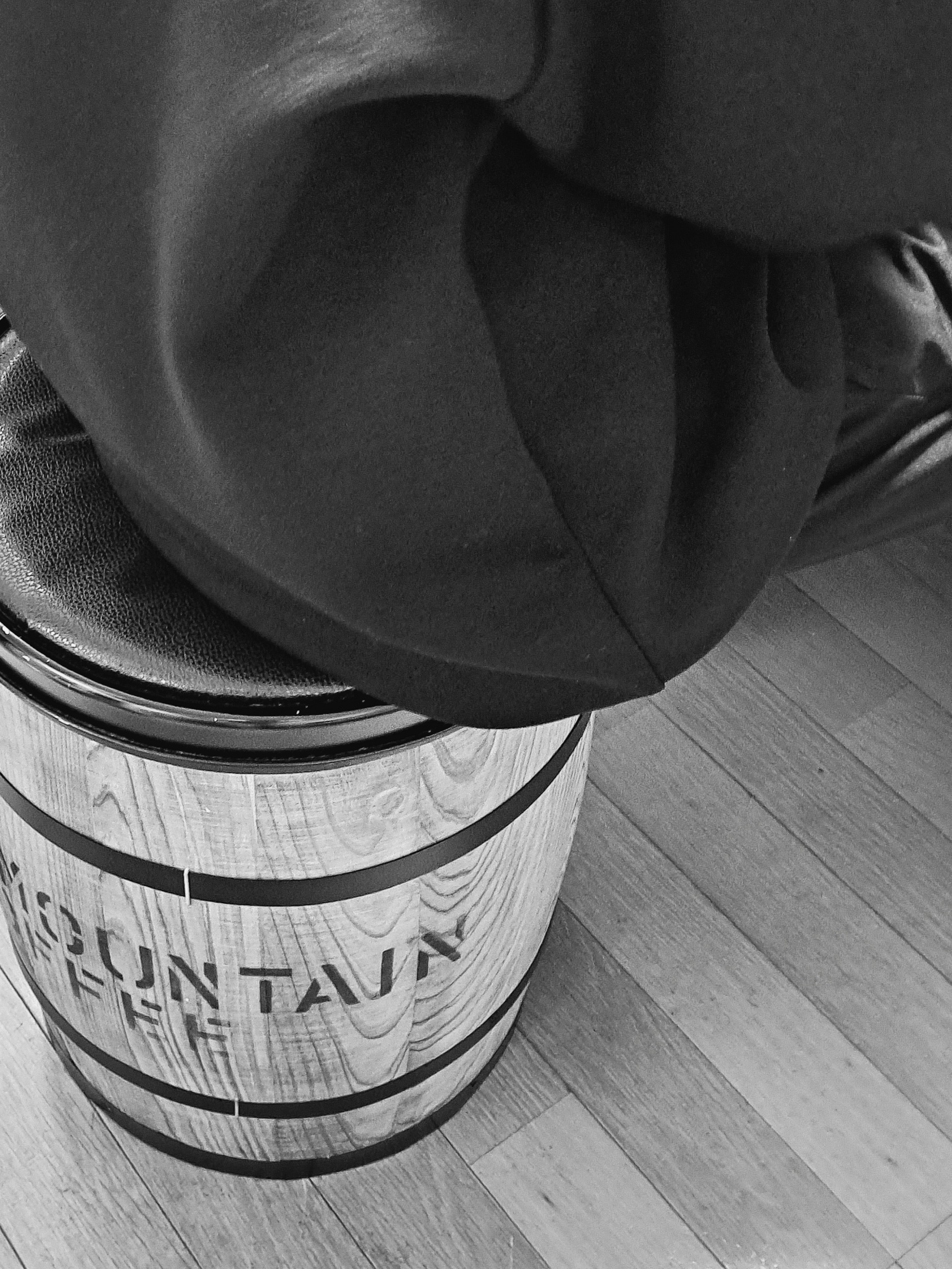 Una persona sentada en un barril etiquetado Mountain Coffee en blanco y negro