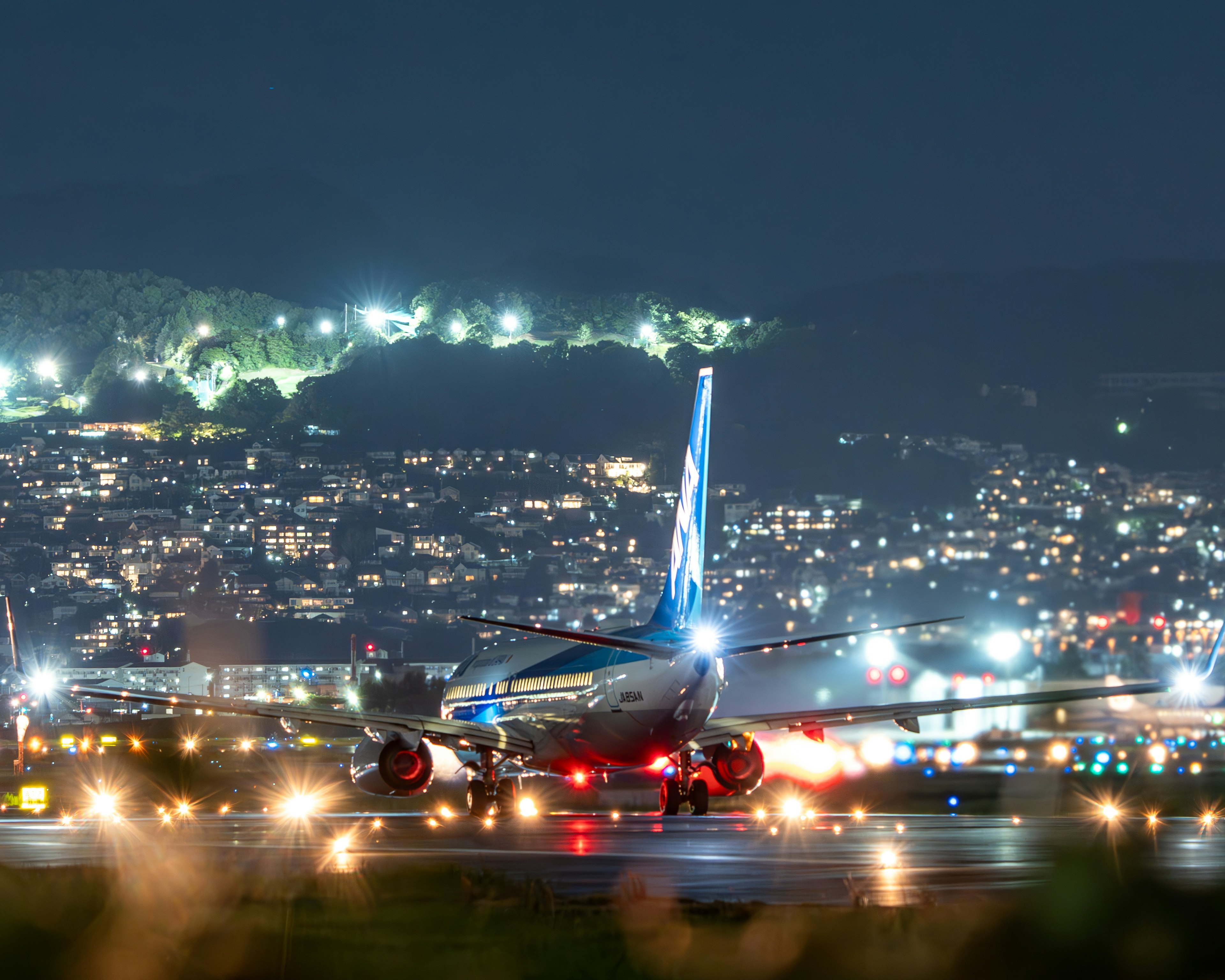 Flugzeug auf der Landebahn bei Nacht mit Stadtlichtern im Hintergrund