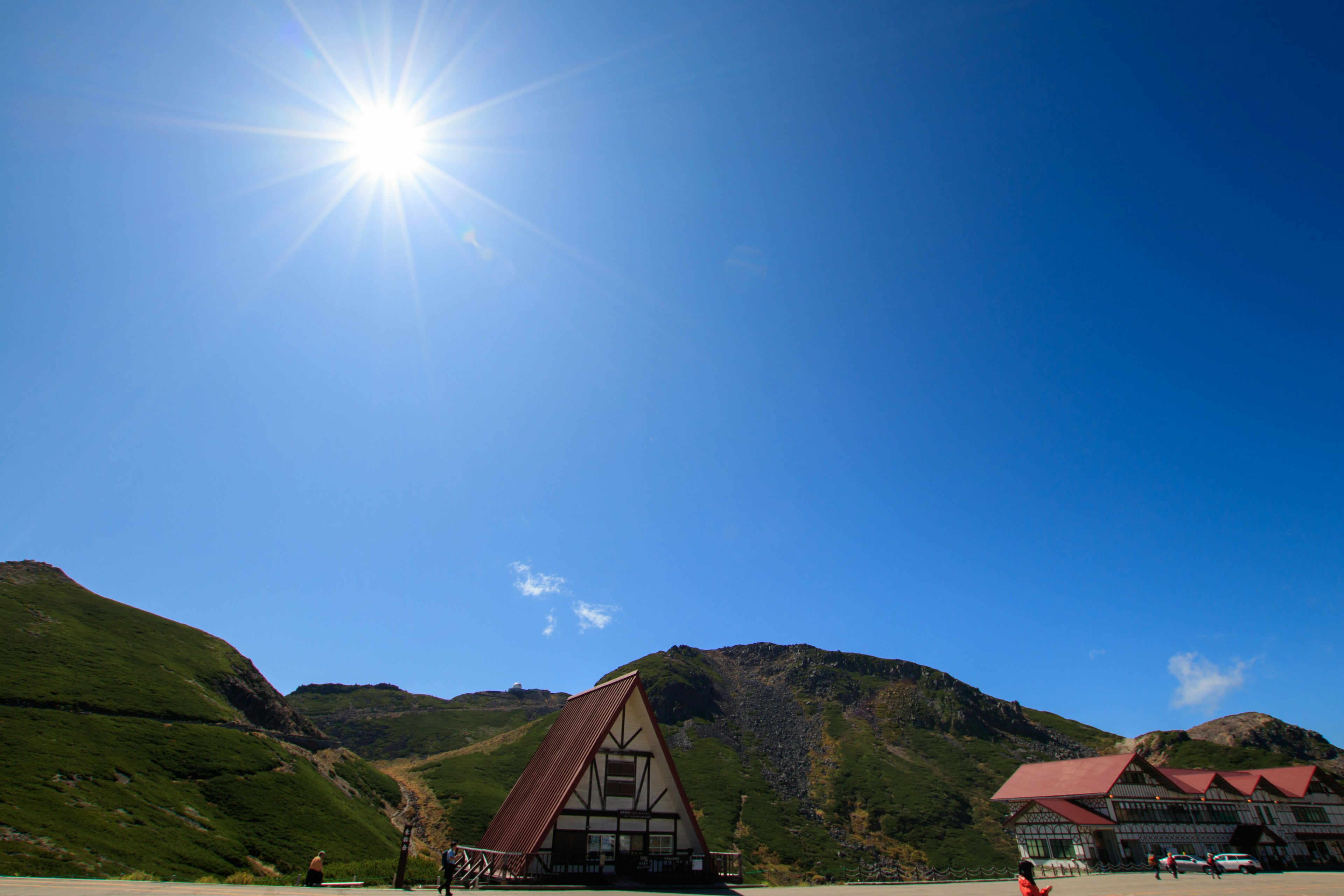 Scenic view with a bright sun over a triangular-roofed building and green hills