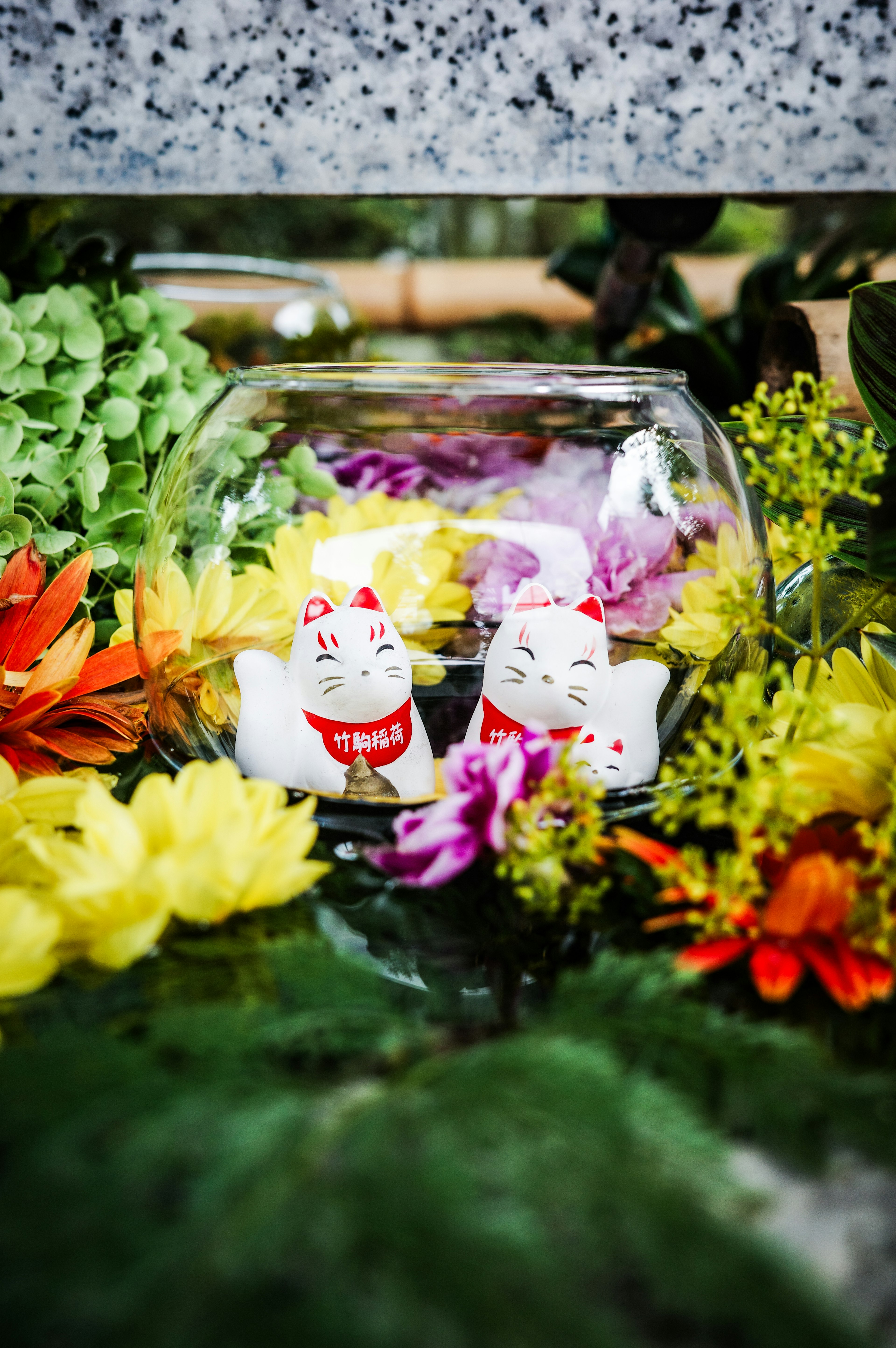 A glass bowl with white cat figurines surrounded by colorful flowers