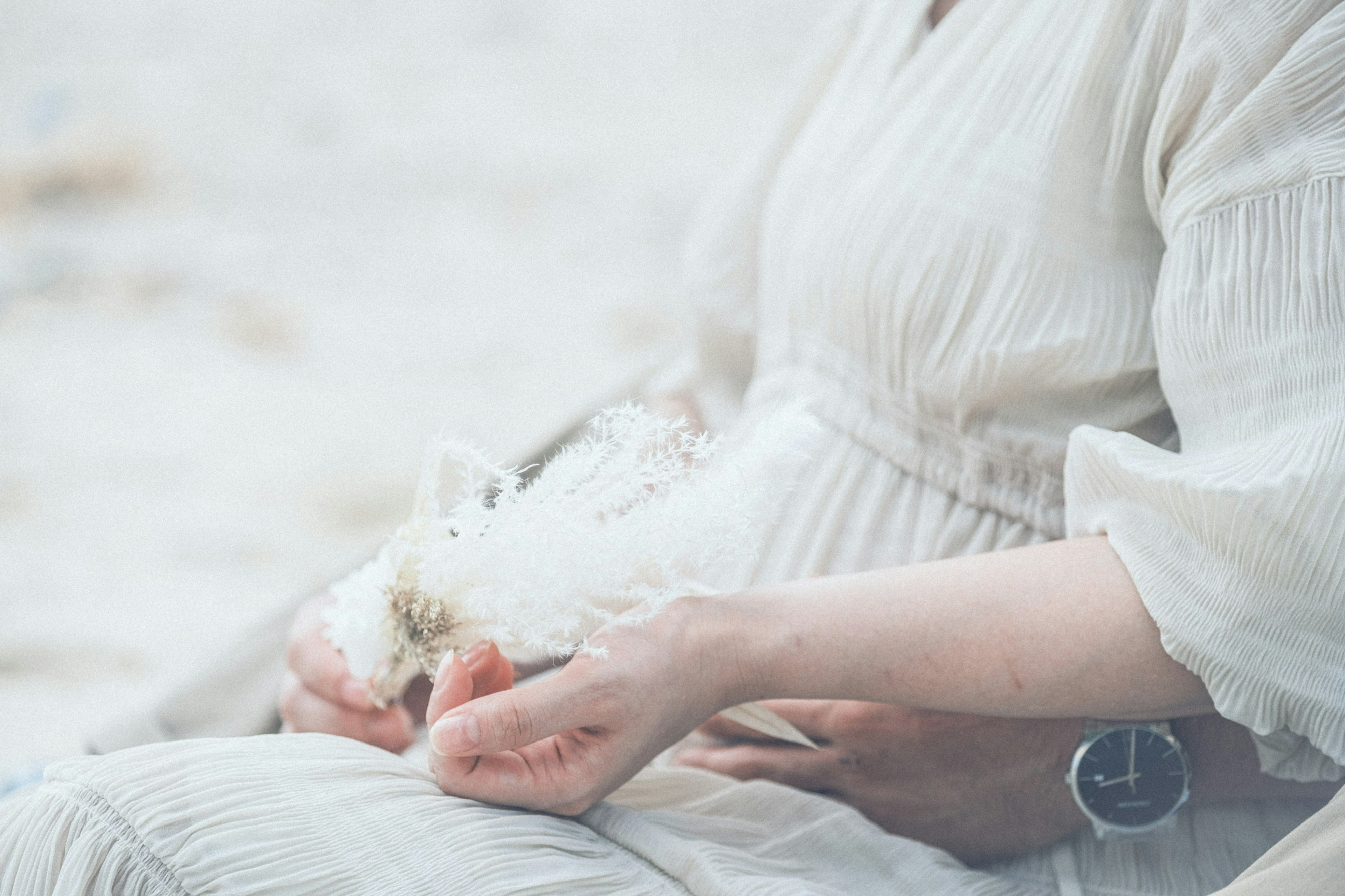 Eine Frau in einem weißen Kleid sitzt am Strand mit den Händen auf ihrem Bauch