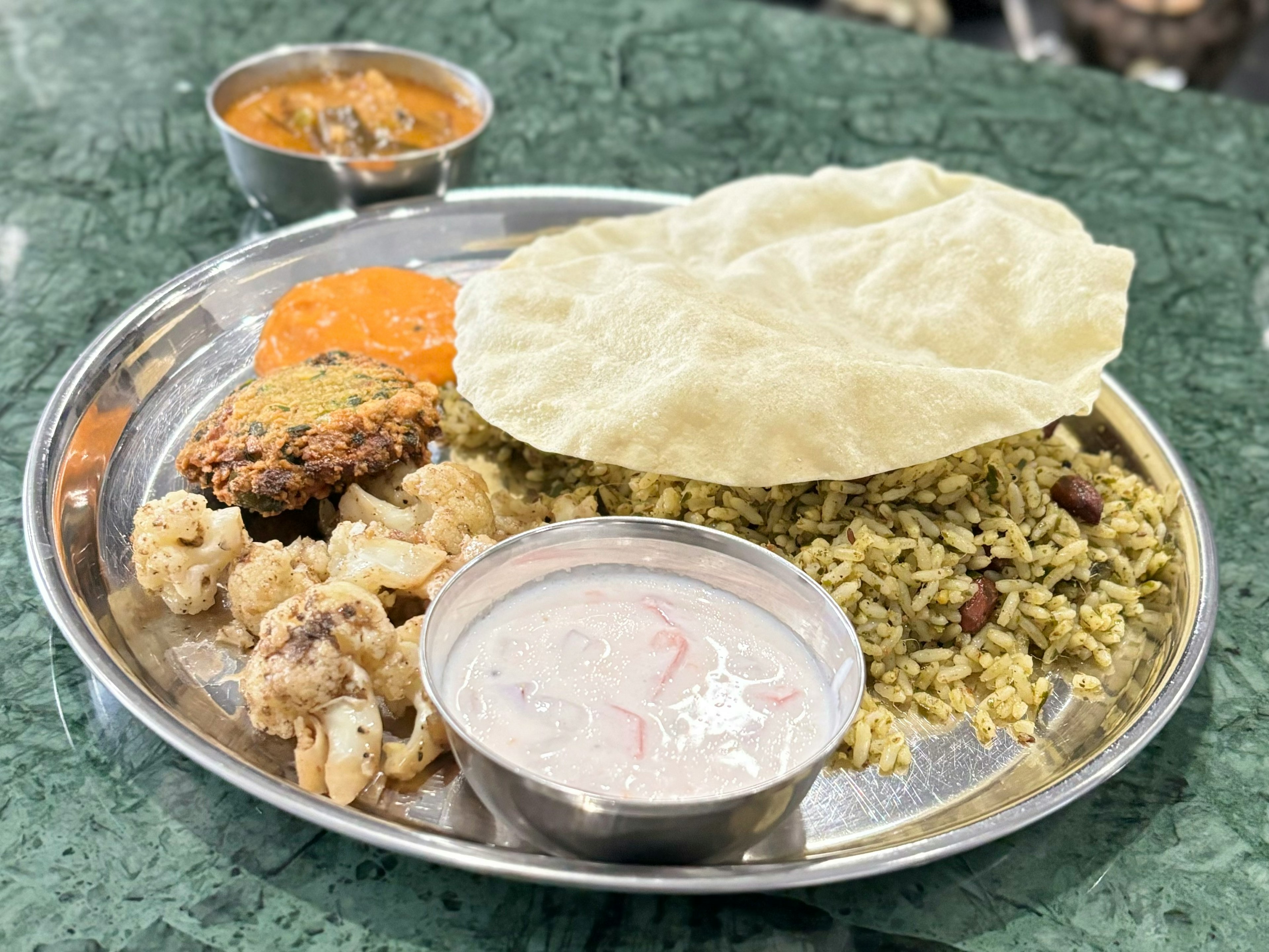 Un plato de cocina india con curry, arroz, papad, yogur y verduras salteadas