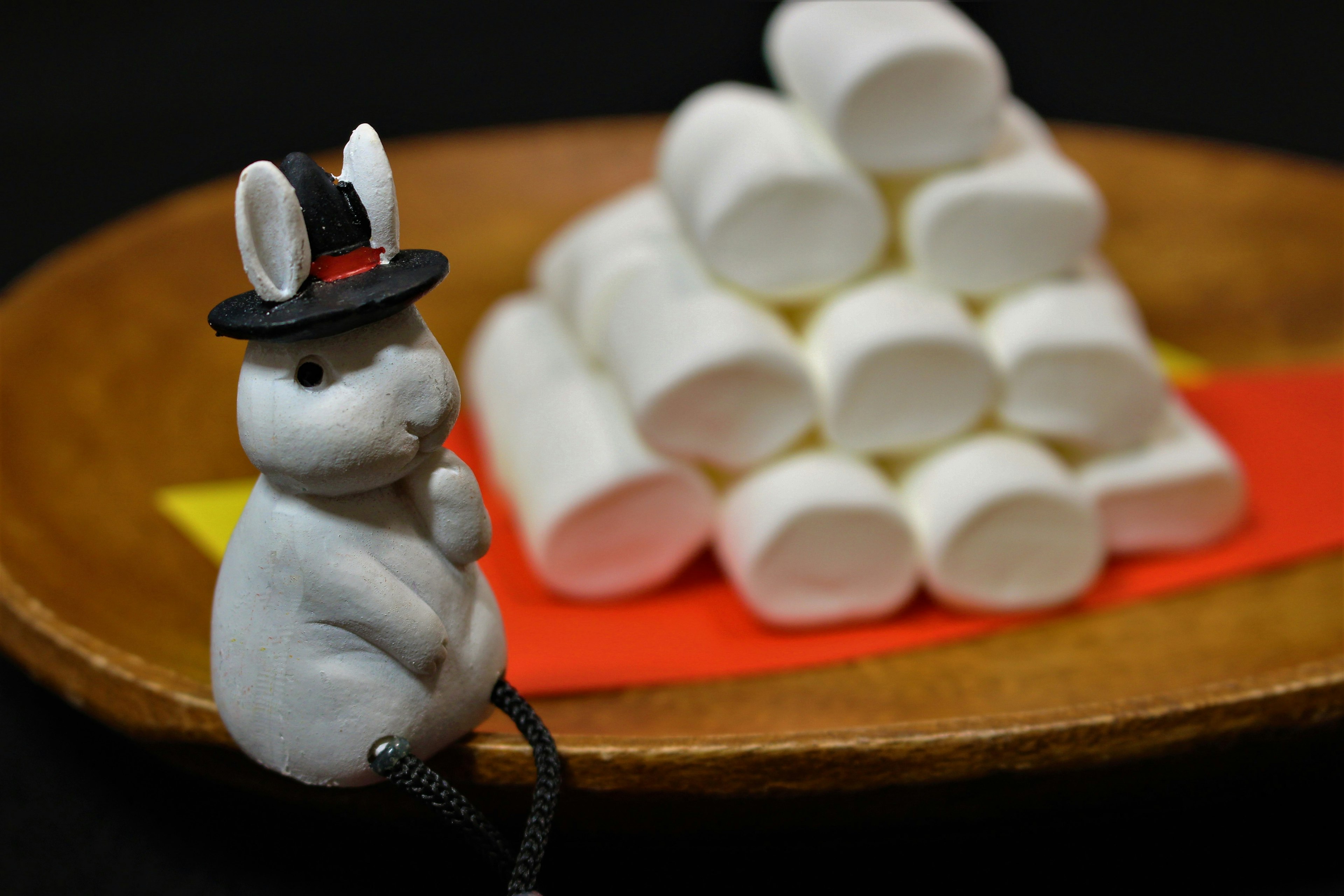 Une figurine de lapin portant un chapeau à côté d'une pyramide de guimauves sur une assiette en bois