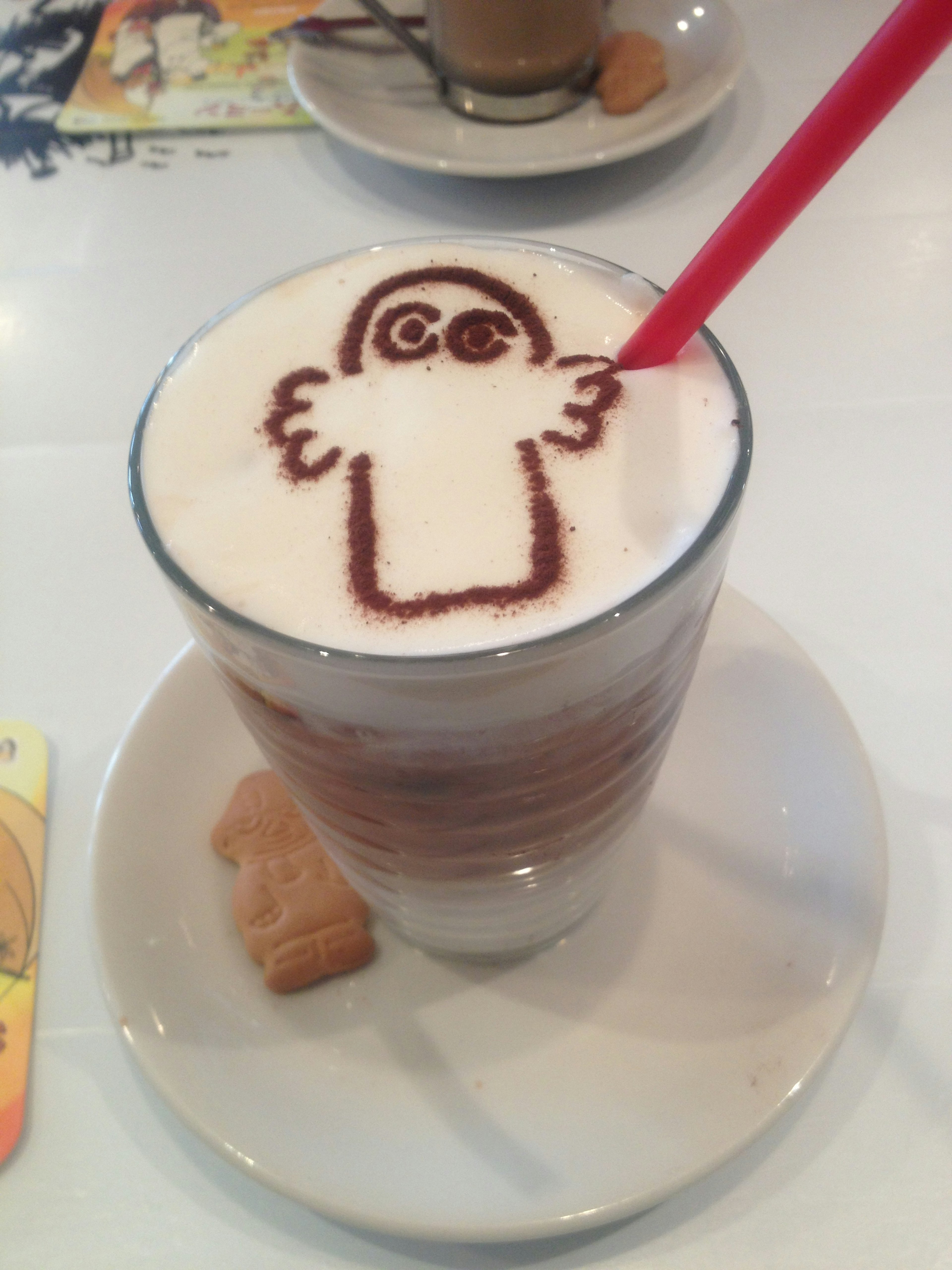 Café latte con arte de latte de fantasma lindo en la parte superior con cacao pajita roja y galleta al lado