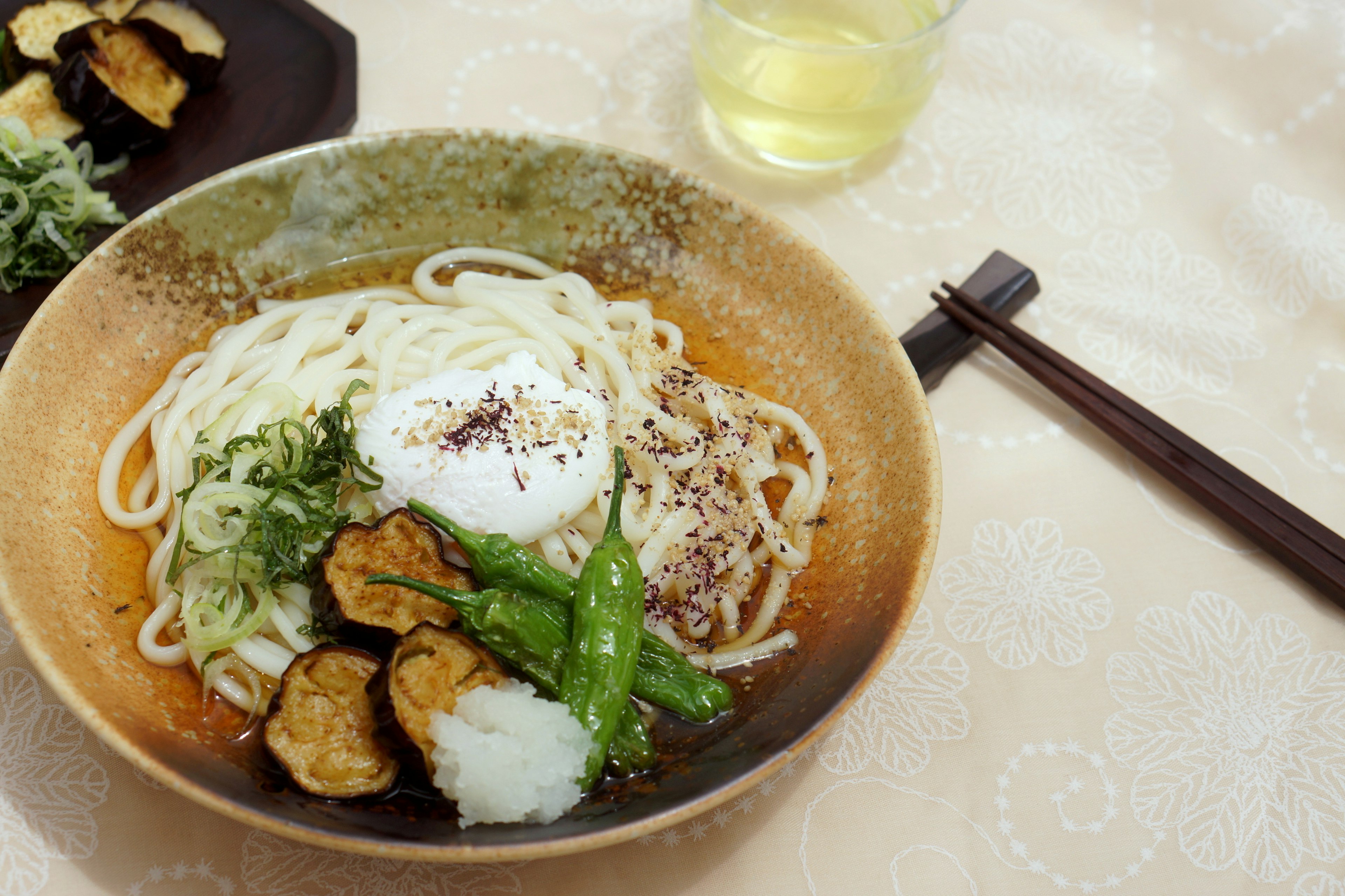 温かいうどんのボウルに生卵と野菜が添えられた料理