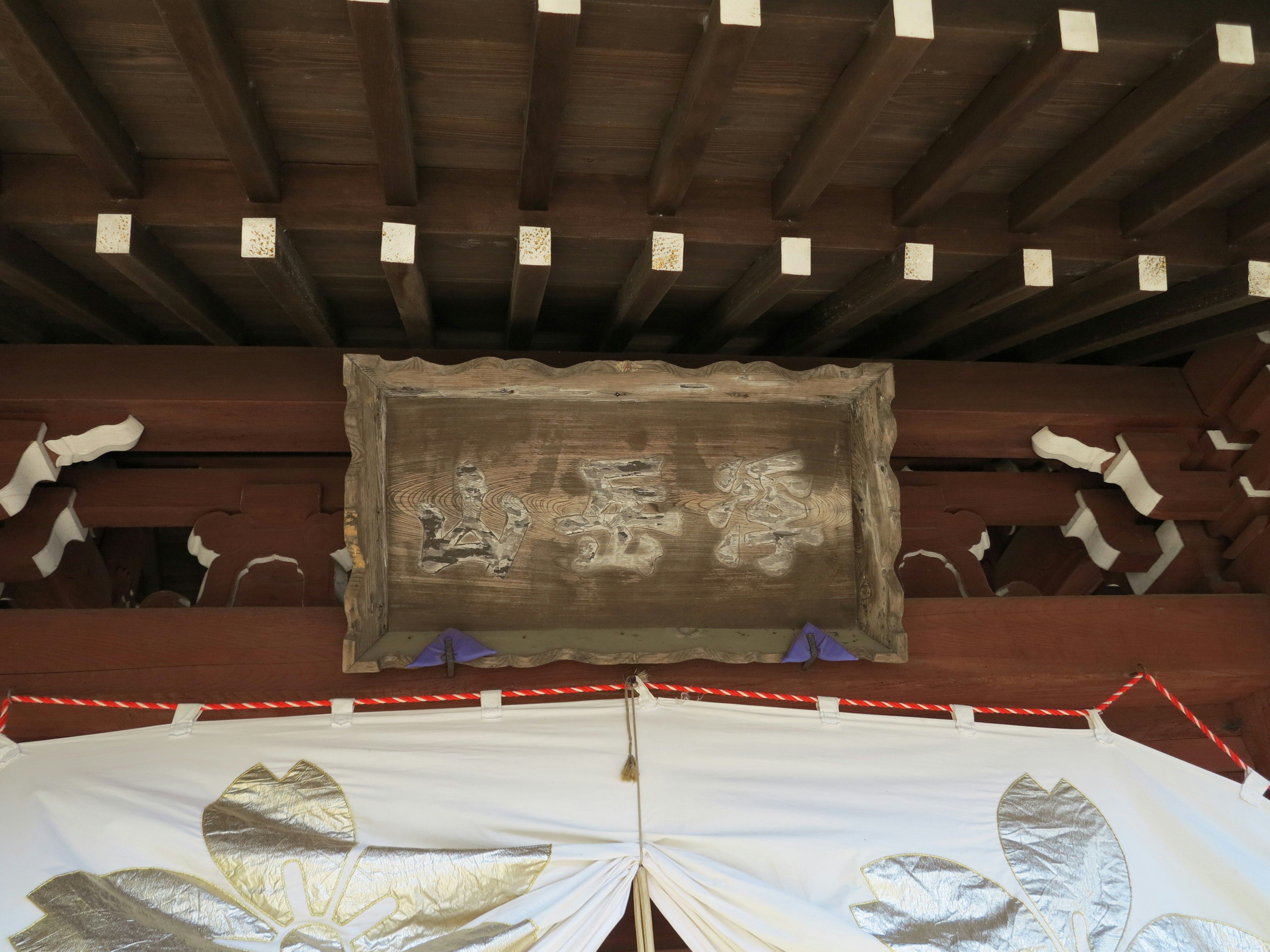 Old wooden sign under the roof of a shrine with white fabric