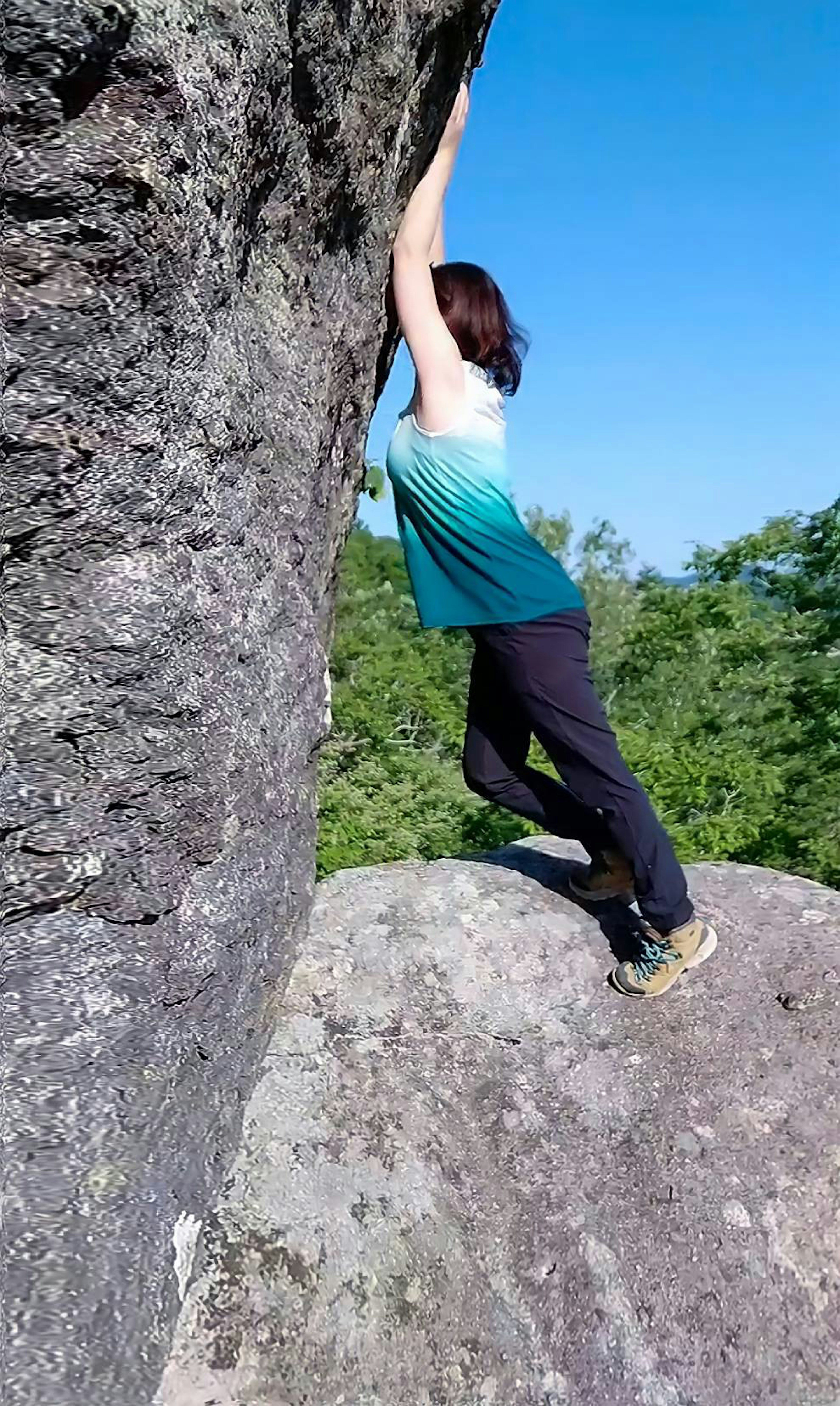 Woman climbing a rock wearing a green shirt