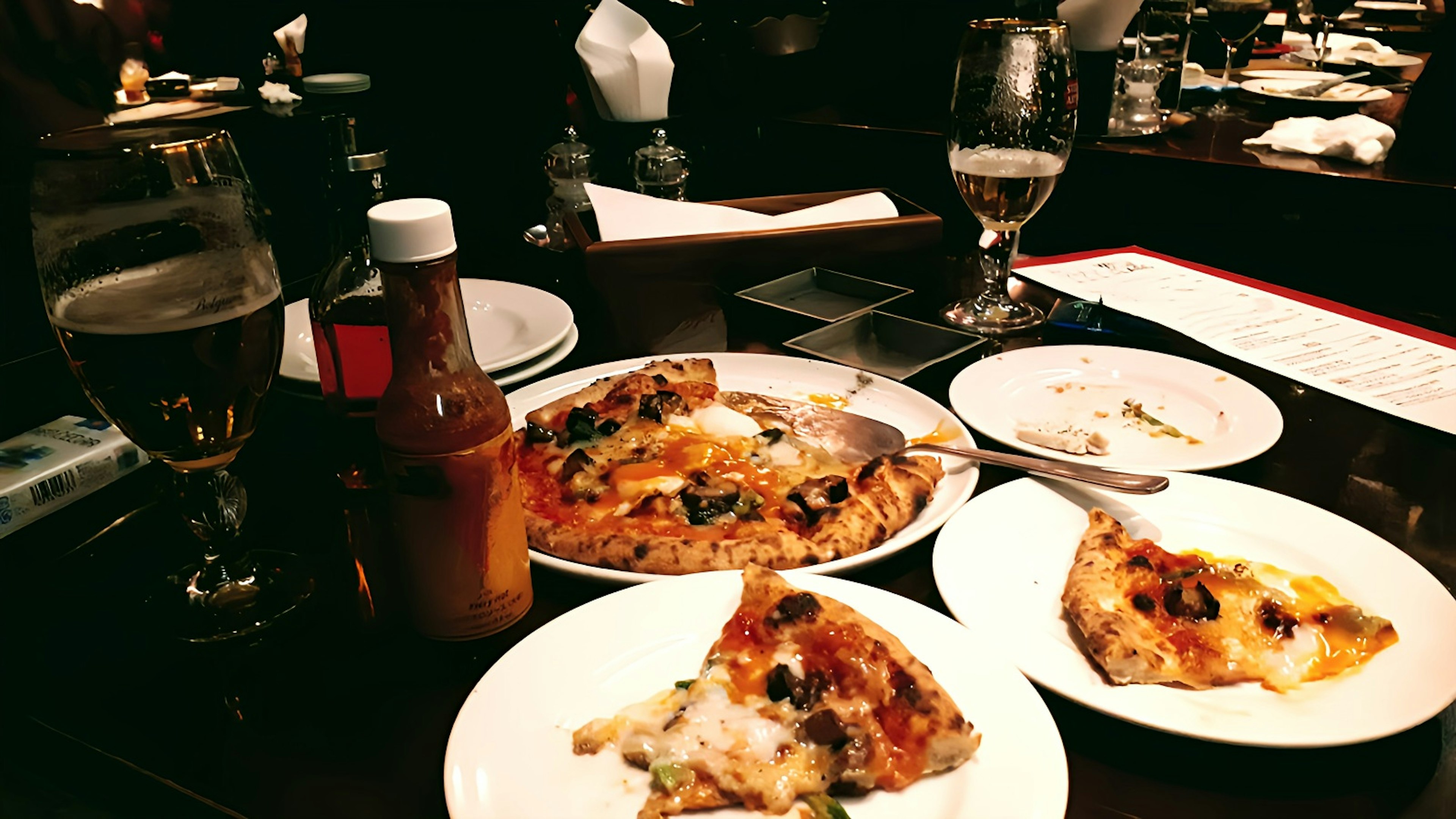 Table with pizza slices and beer glasses partially eaten food and condiments visible