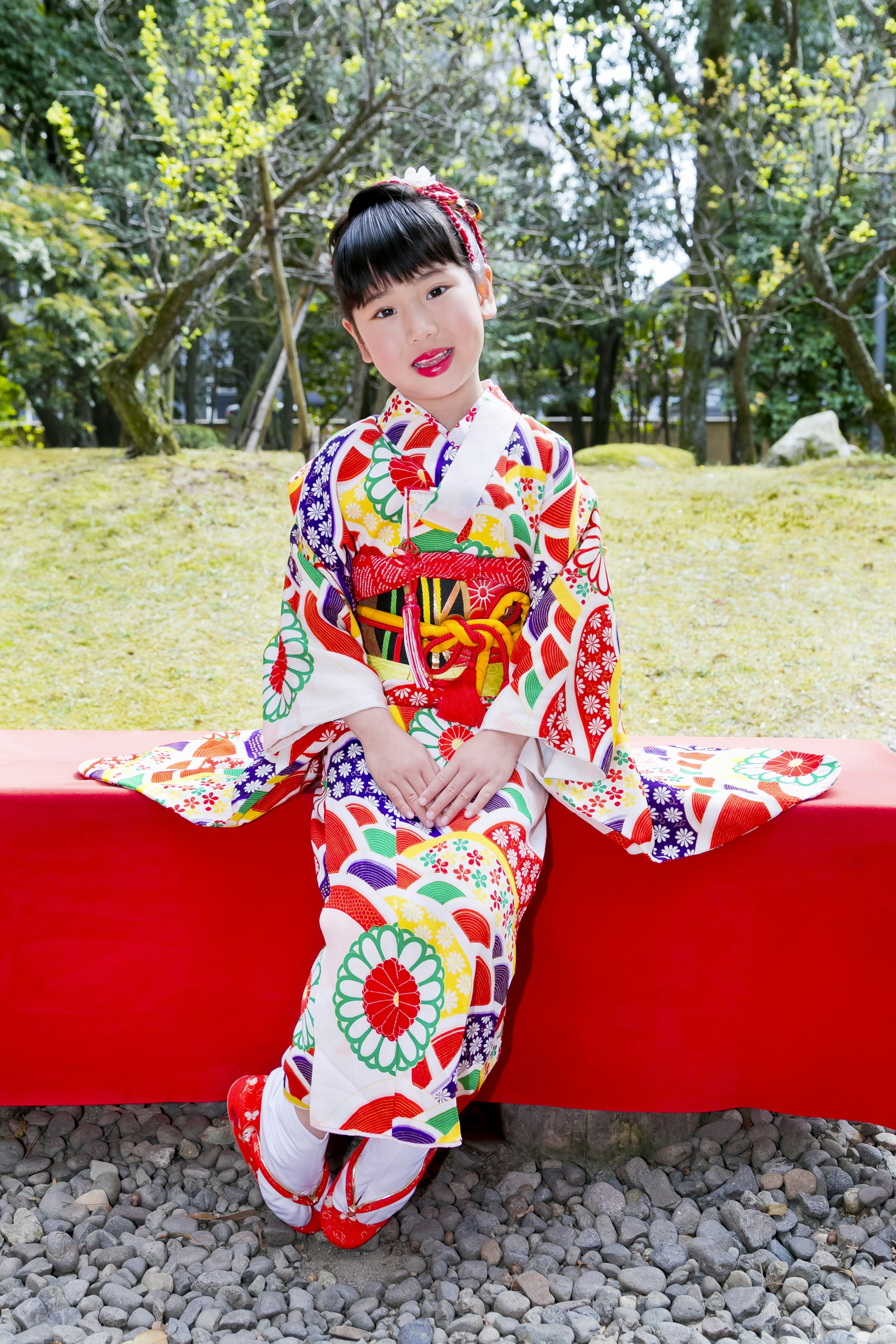 Seorang gadis dalam kimono berwarna-warni duduk di bangku merah tersenyum