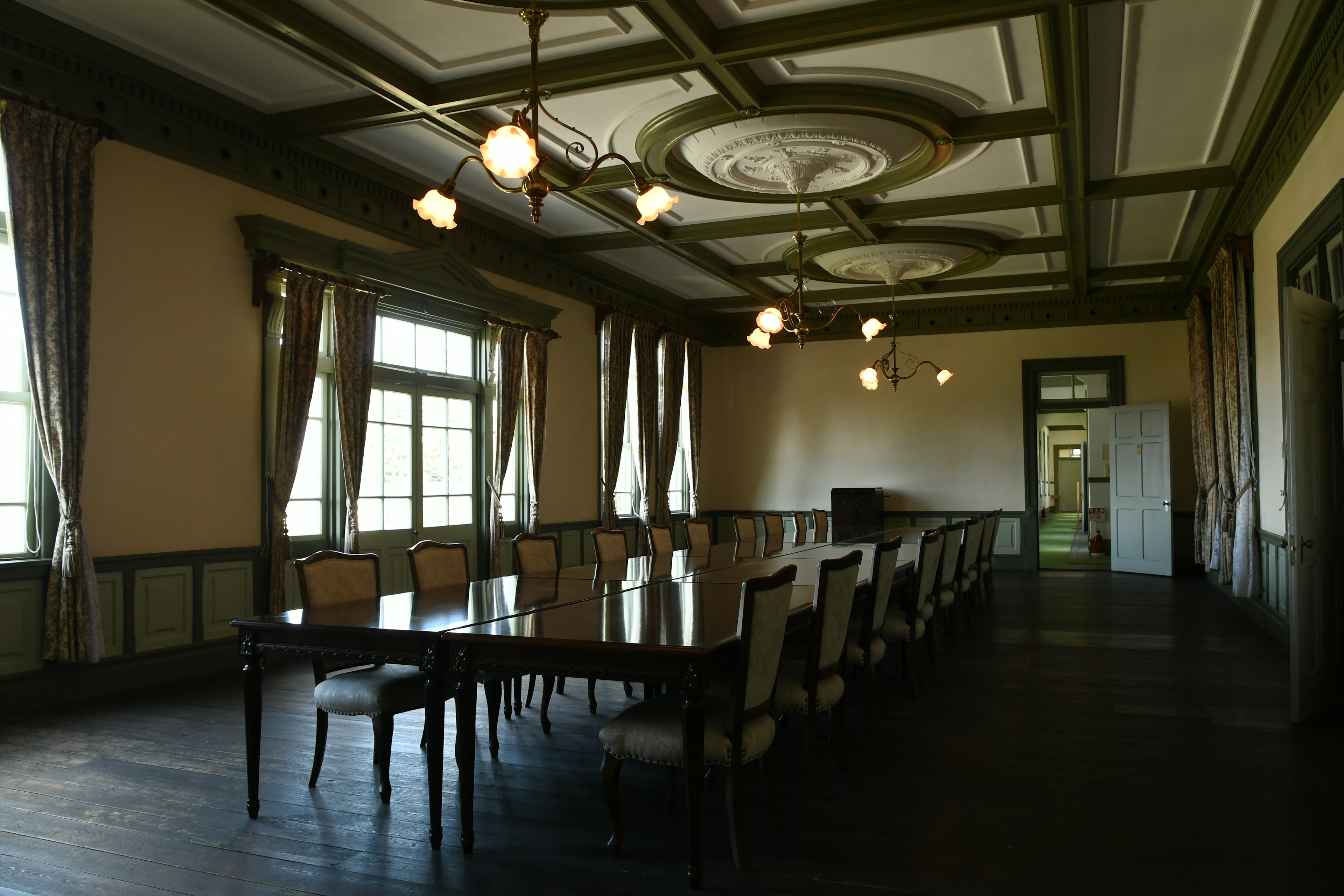 Interno spazioso di una sala conferenze con lungo tavolo e sedie illuminazione a lampadario e luce naturale dalle finestre