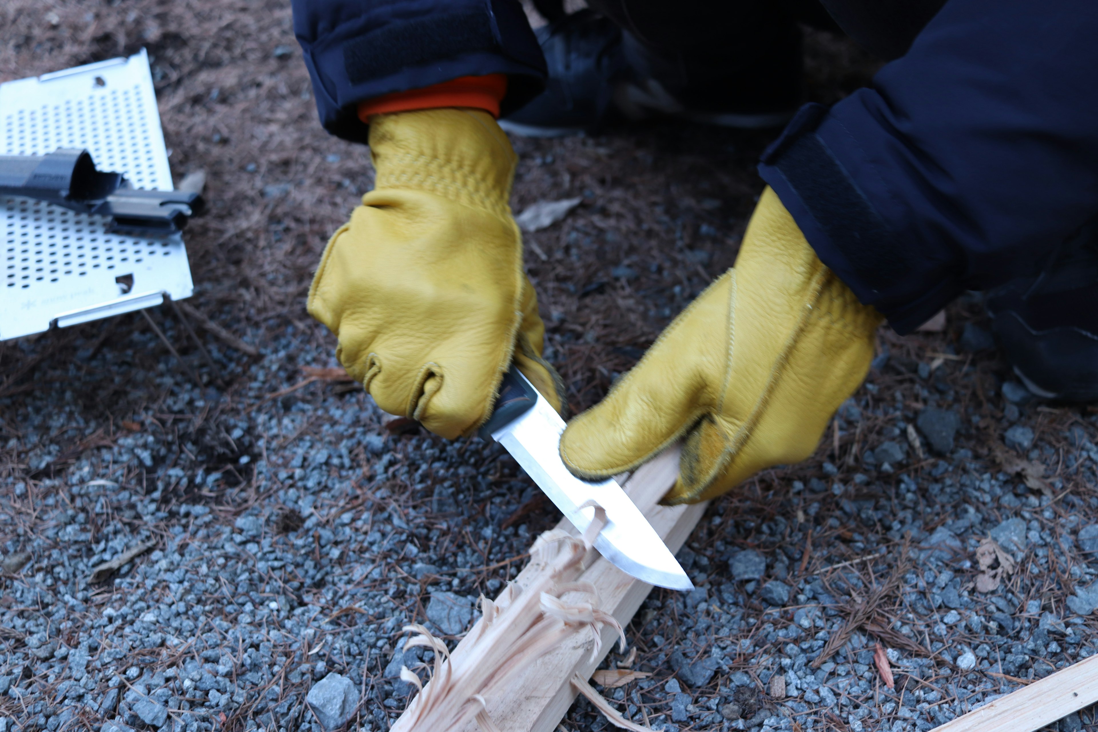 Eine behandschuhte Hand, die ein Messer zum Schnitzen von Holz benutzt