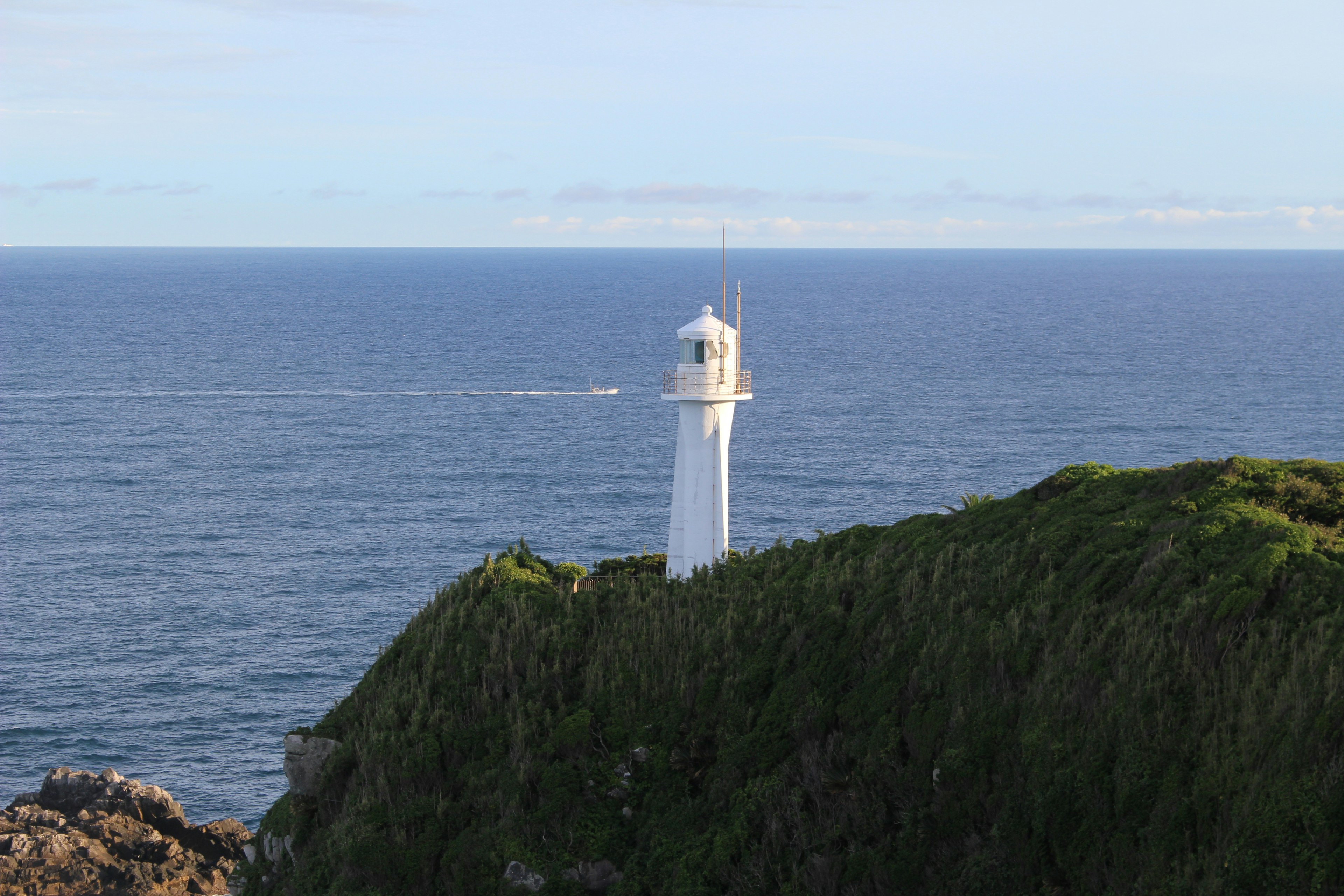 White lighthouse on a green cliff overlooking the ocean