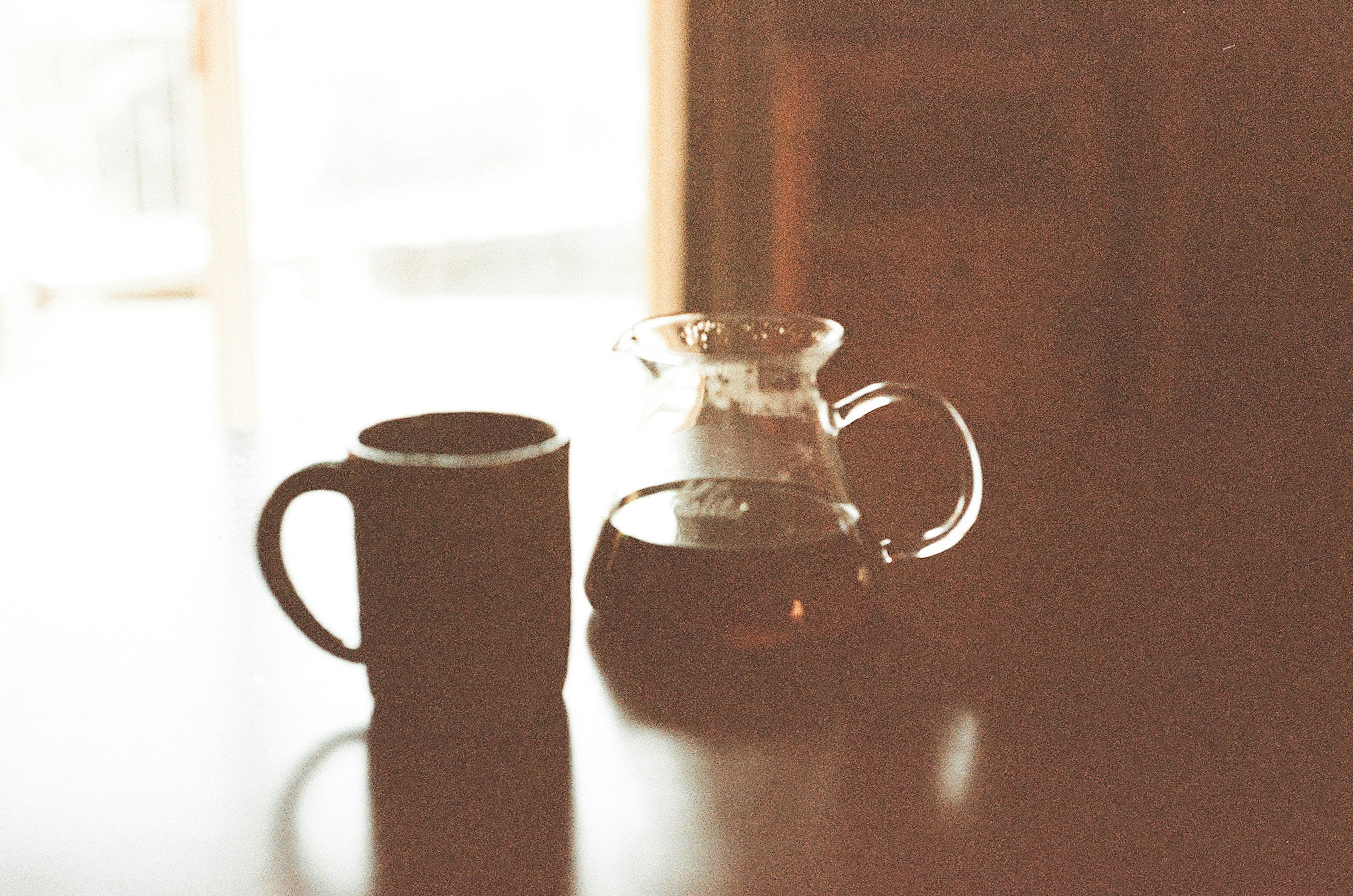 Eine Kaffeekanne und eine Tasse auf einem Tisch neben einem Fenster